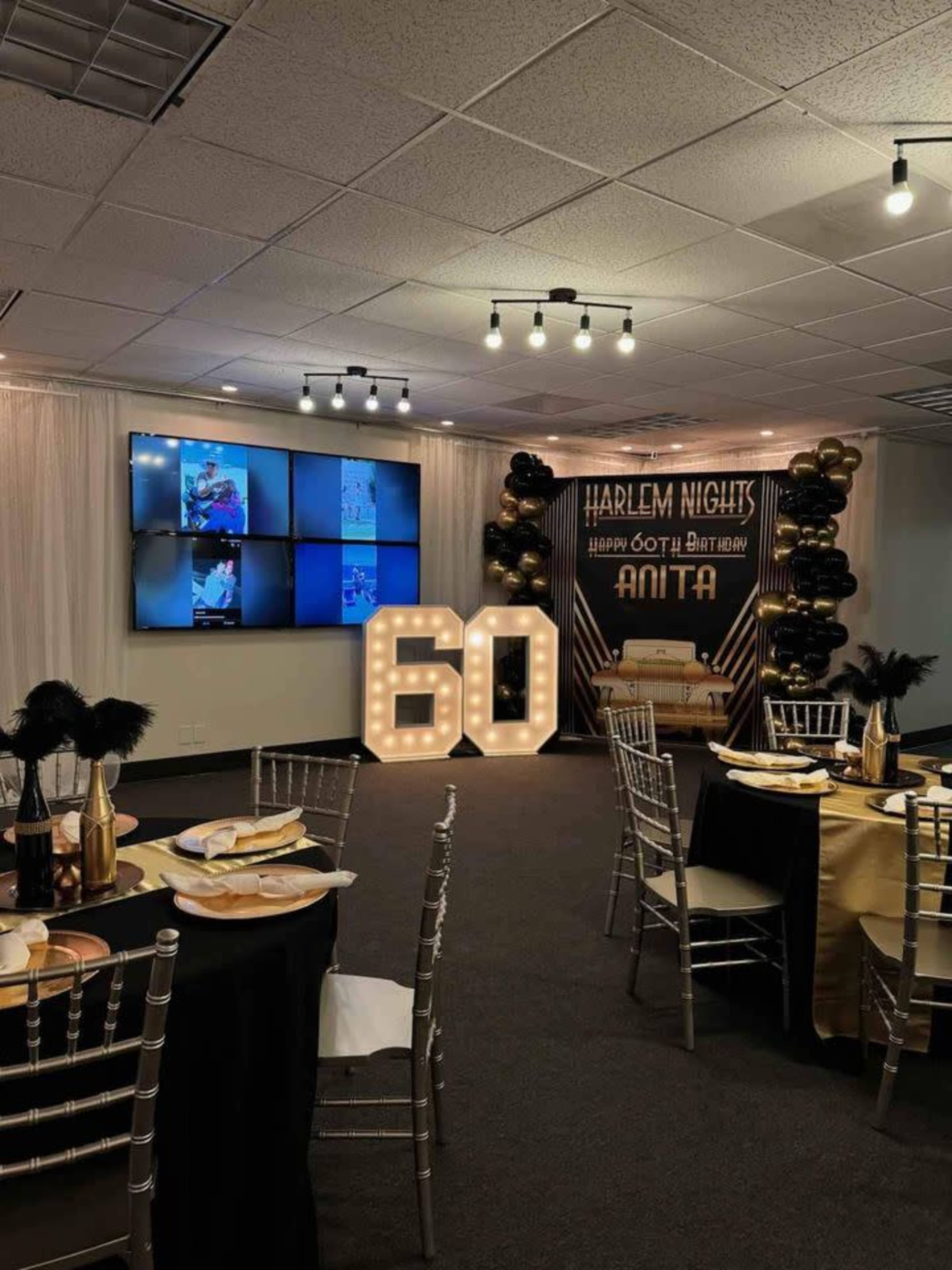 The image shows a decorated event space for a 60th birthday celebration, featuring a large illuminated "60," gold and black decor, a seating area, and screens displaying photos.