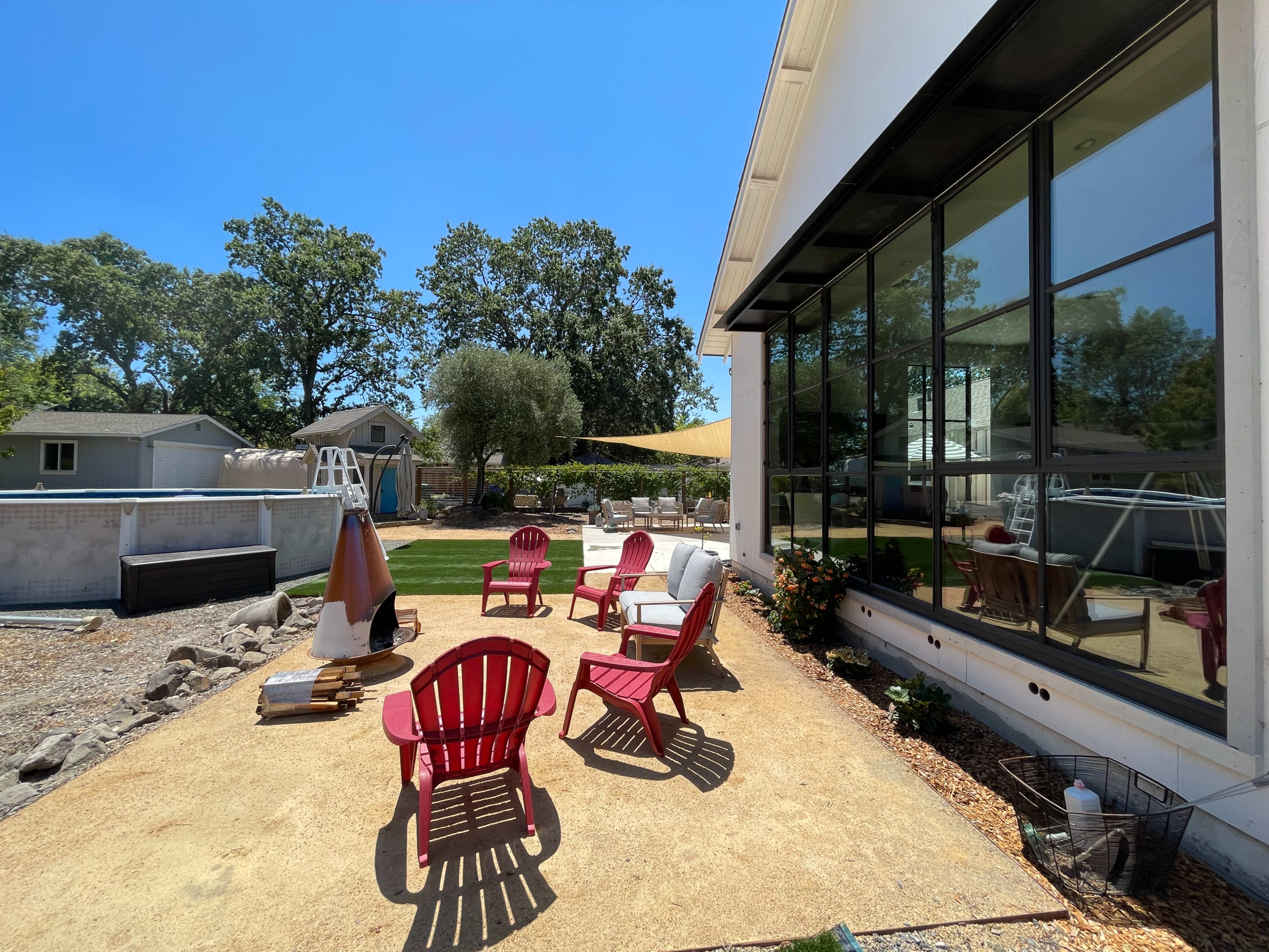 A patio area features red chairs, a cone-shaped structure, and a backdrop of green trees and a spacious yard.