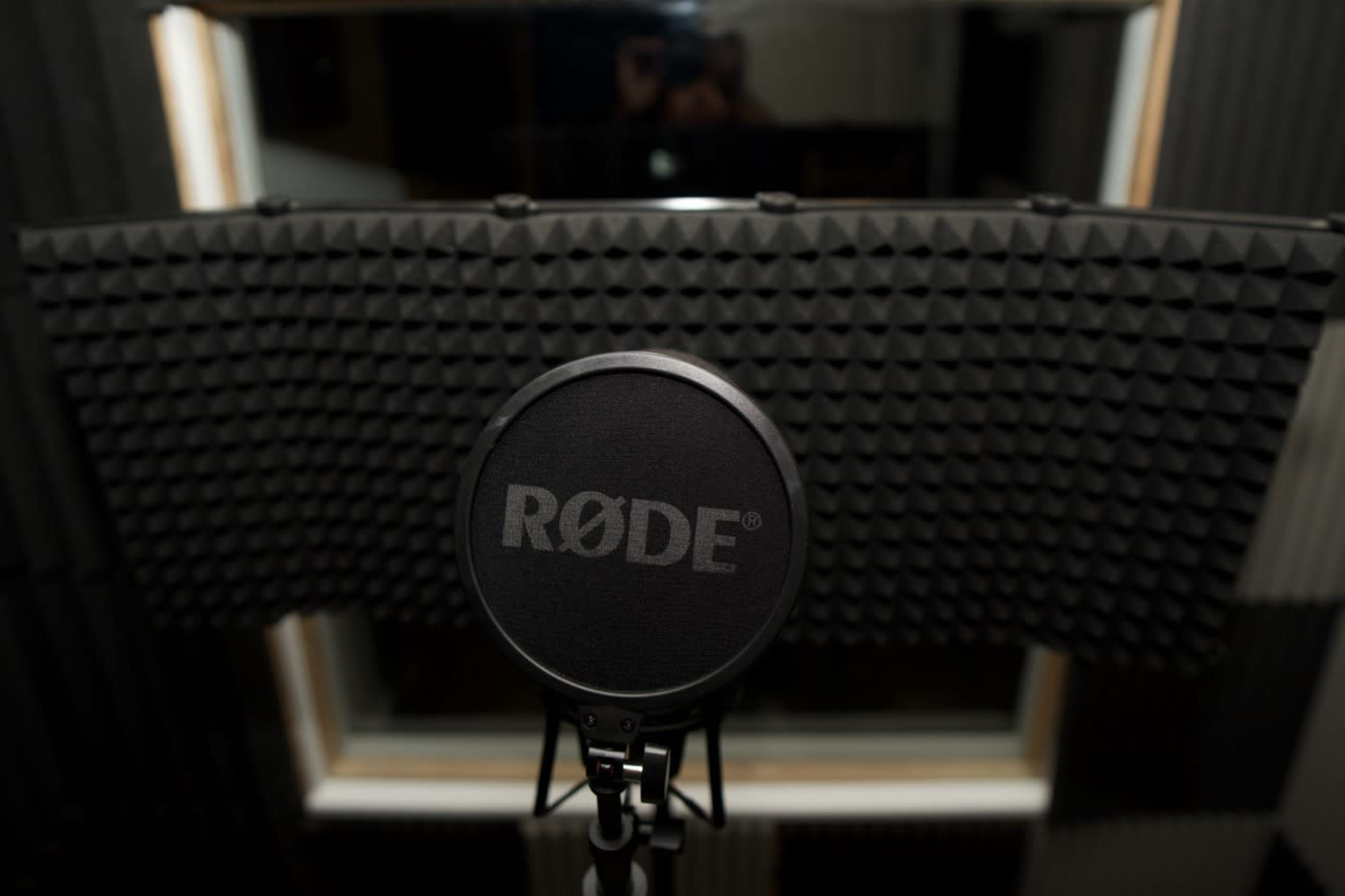 A microphone with a pop filter is positioned in front of soundproofing panels in a recording studio.