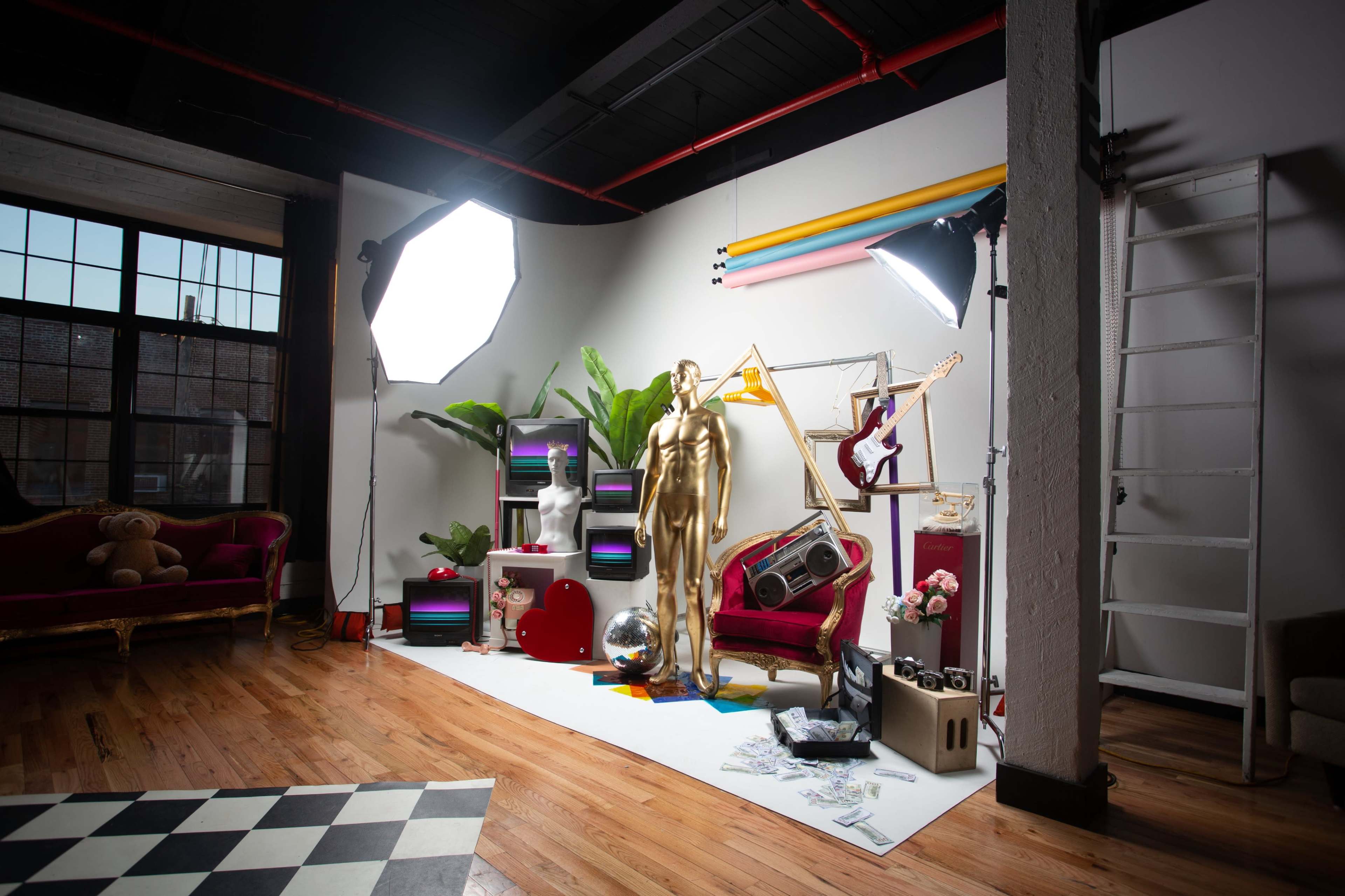 The image shows a creatively designed studio space featuring a golden mannequin, colorful decor, various musical instruments, and large light sources.