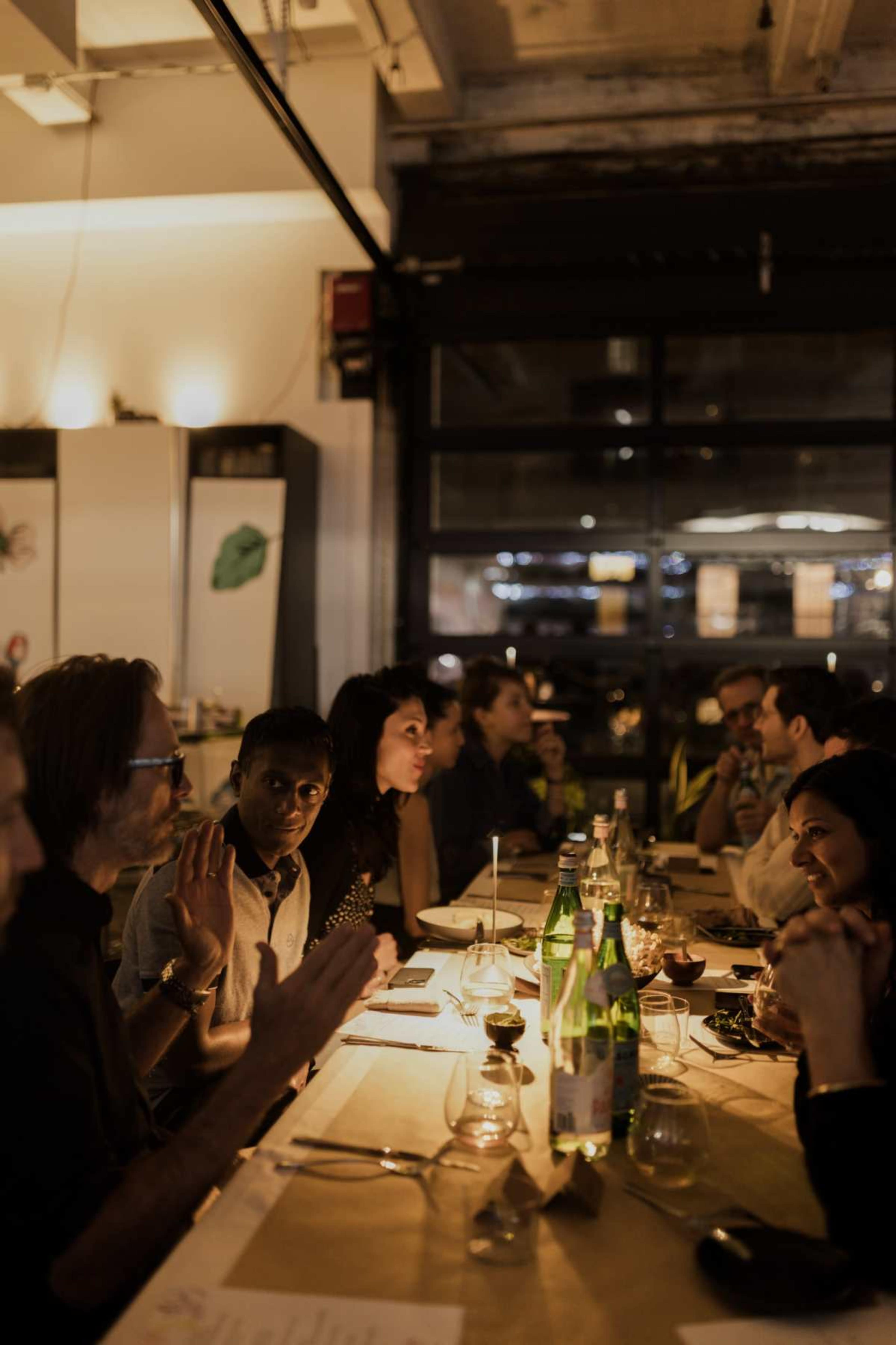 A group of people gathered around a dining table in a softly lit restaurant, engaged in conversation.