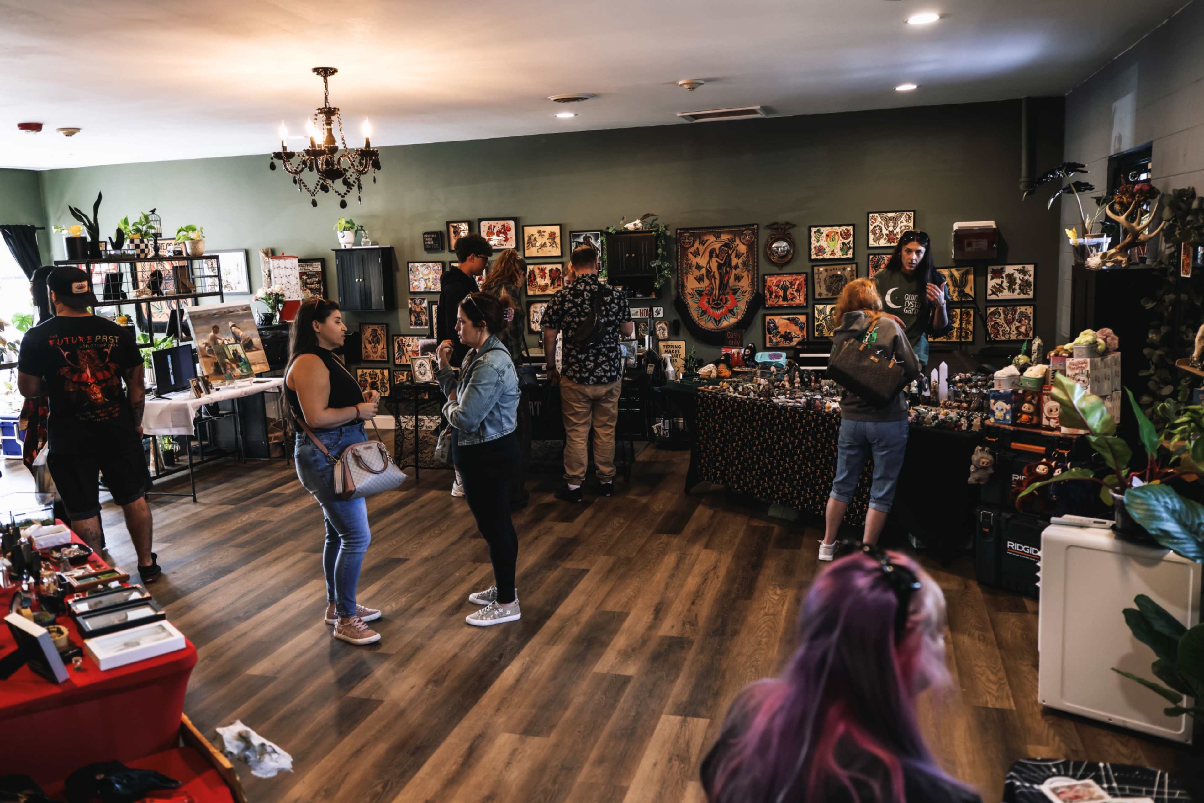 A group of people browse artwork and merchandise in a lively tattoo shop decorated with various framed designs on the walls.
