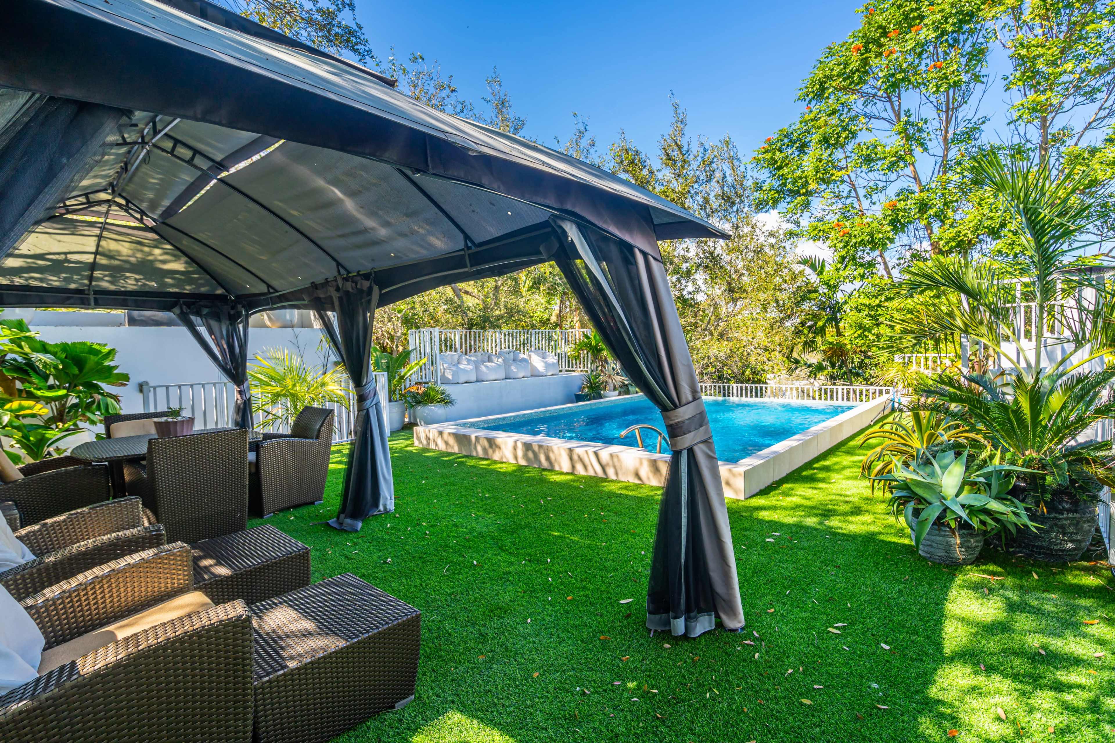A patio area with outdoor seating next to a swimming pool surrounded by greenery.