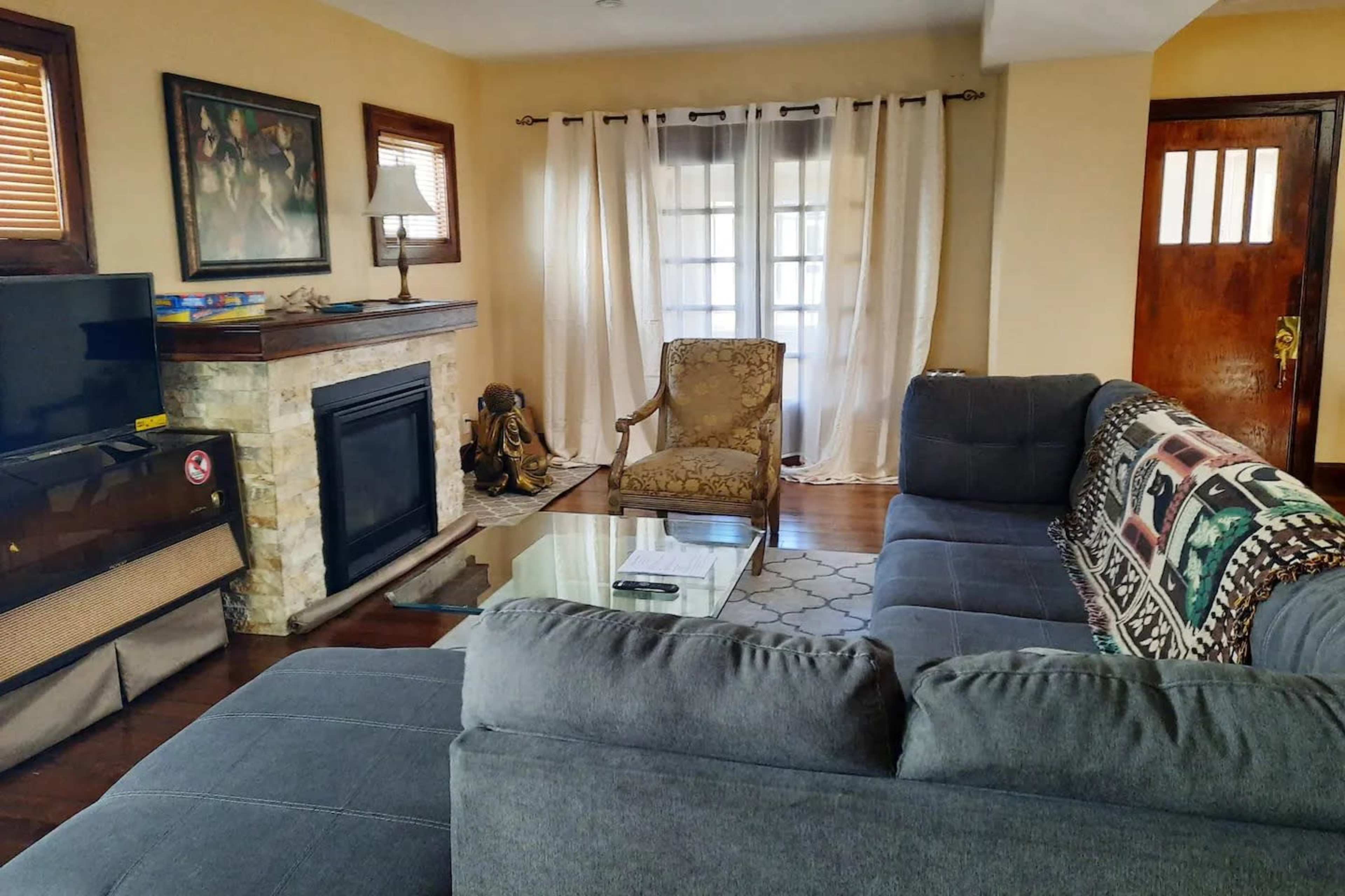 The living room features a gray sectional sofa, a glass coffee table, and a decorative armchair, with a fireplace and a TV against the wall.