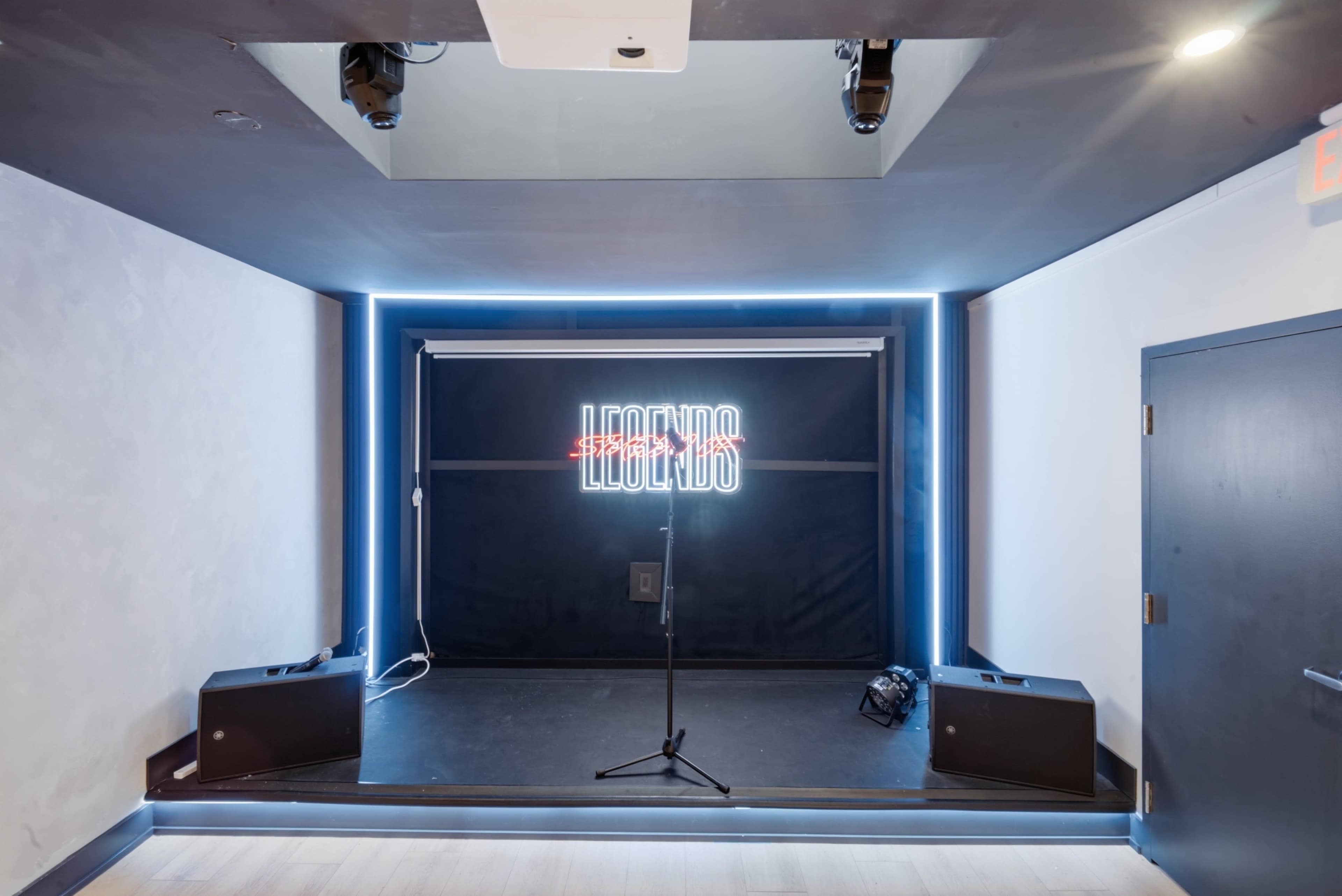 The image shows a small stage area with a microphone stand, illuminated by neon lights that spell "LEGENDS."