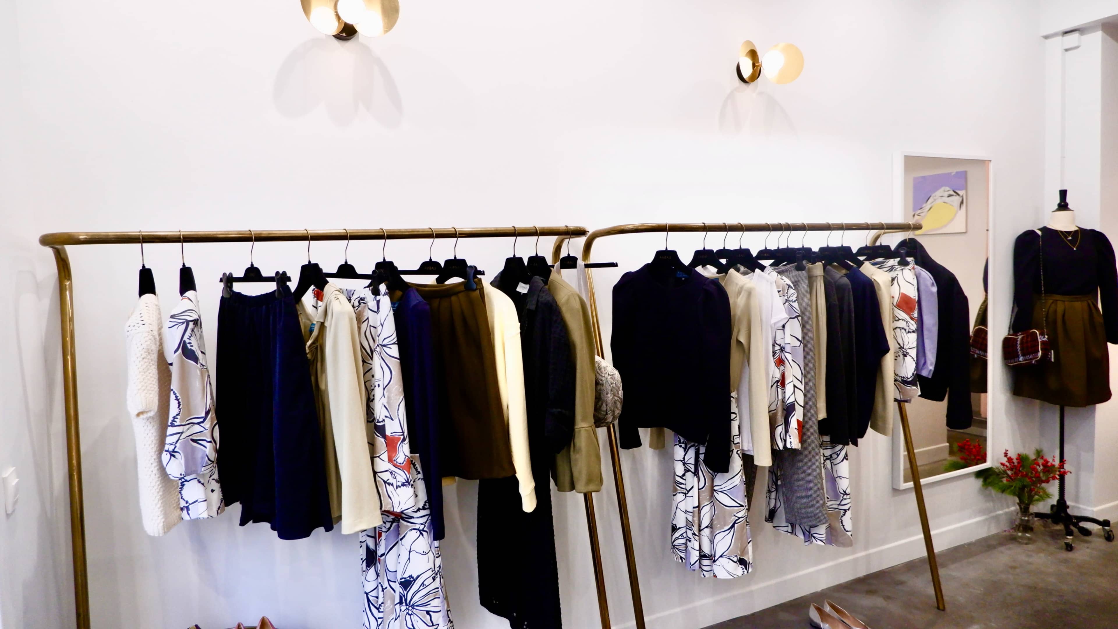A clothing display with a variety of garments hanging on gold clothing racks against a white wall.