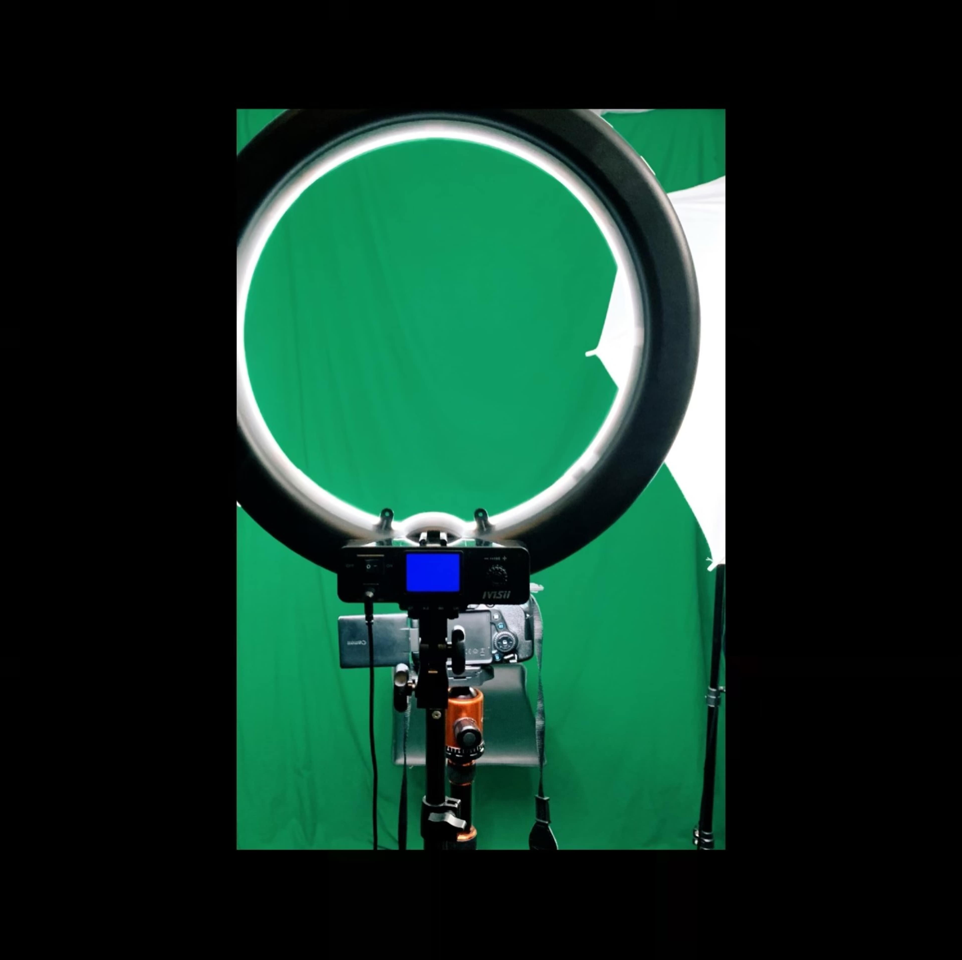 A camera is positioned in front of a ring light with a green backdrop in the background.