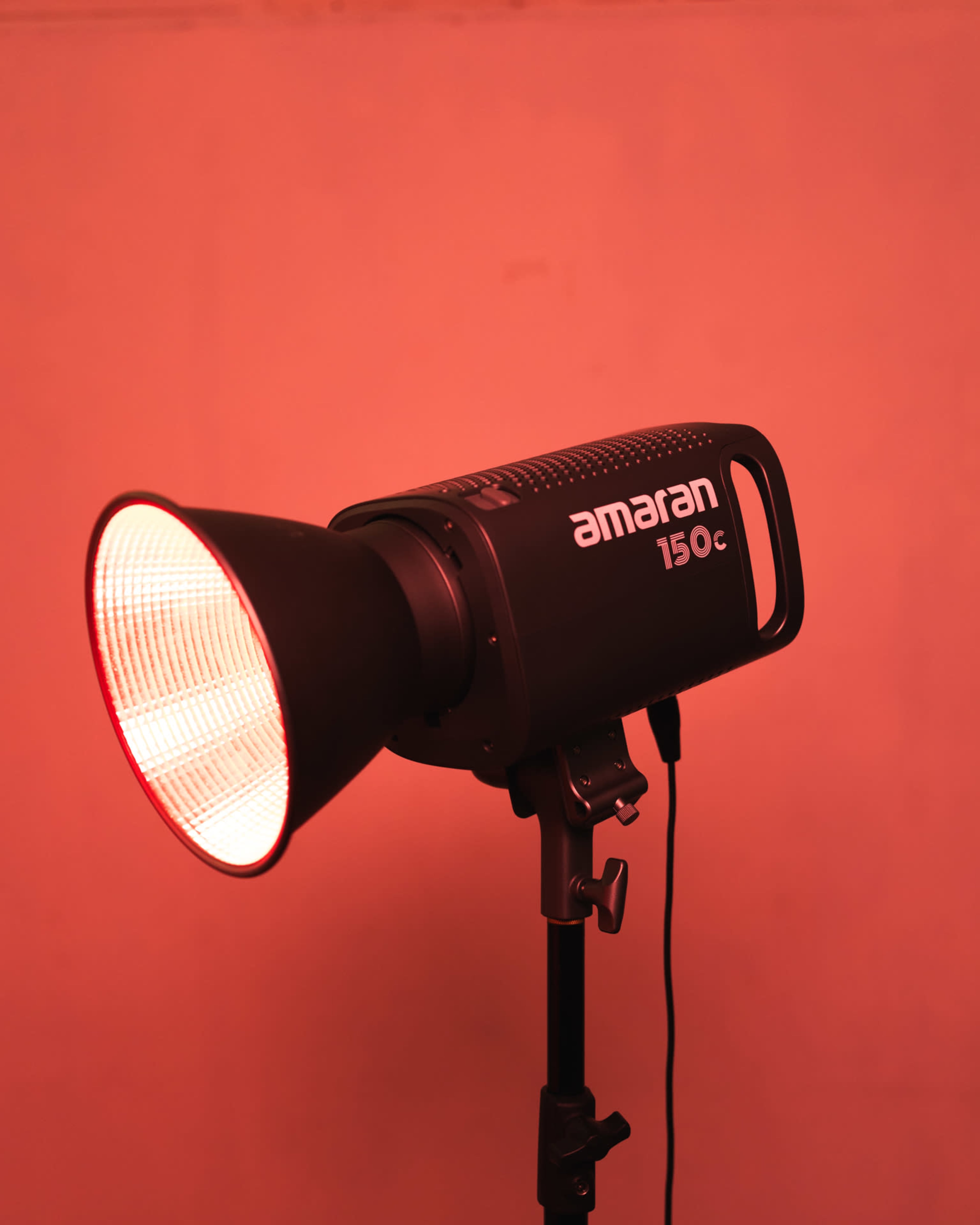 A studio light with a softbox is positioned on a stand, emitting a red glow against a plain background.