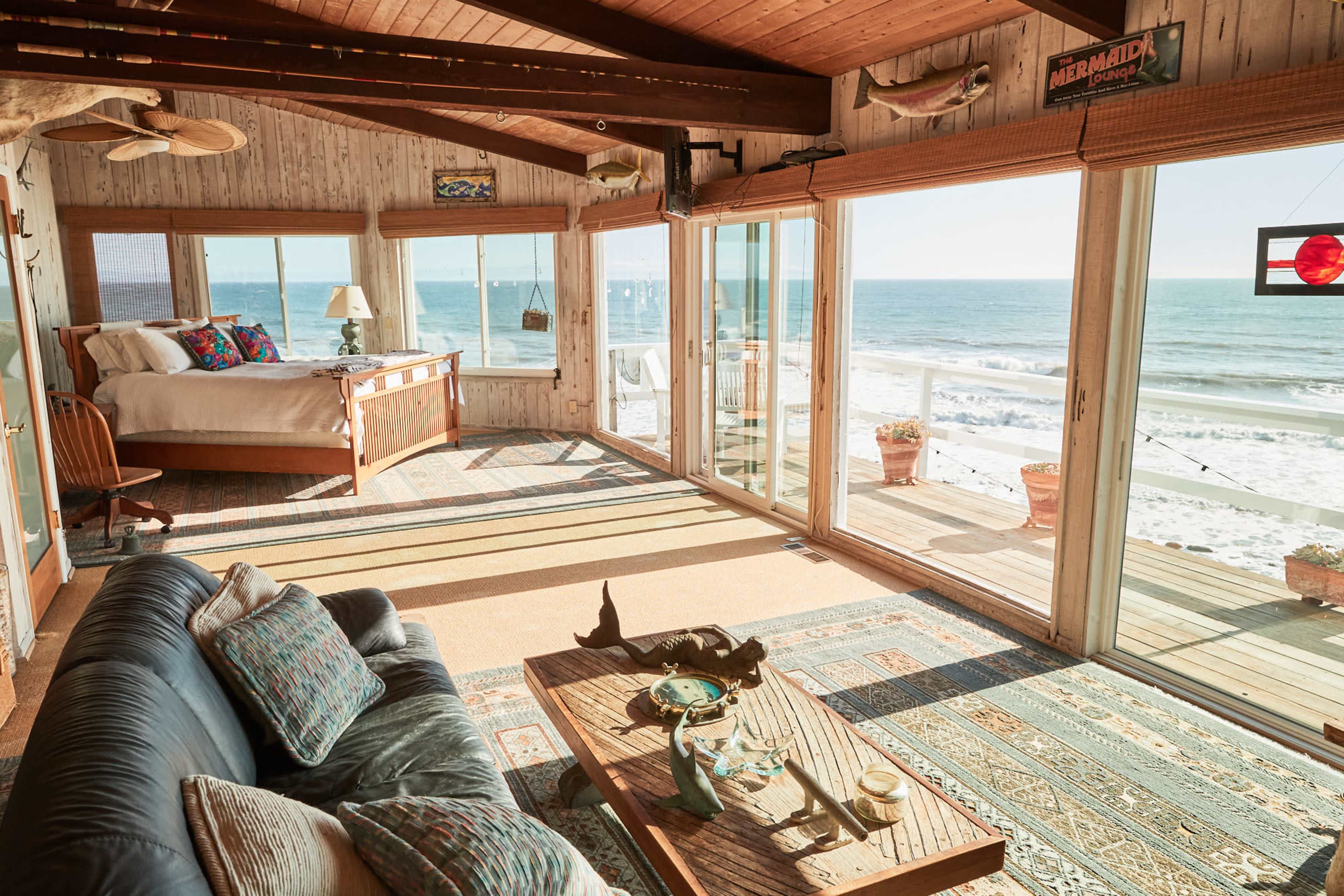 A cozy beachfront room with large glass doors overlooking the ocean, featuring a bed, sofa, and a coffee table.