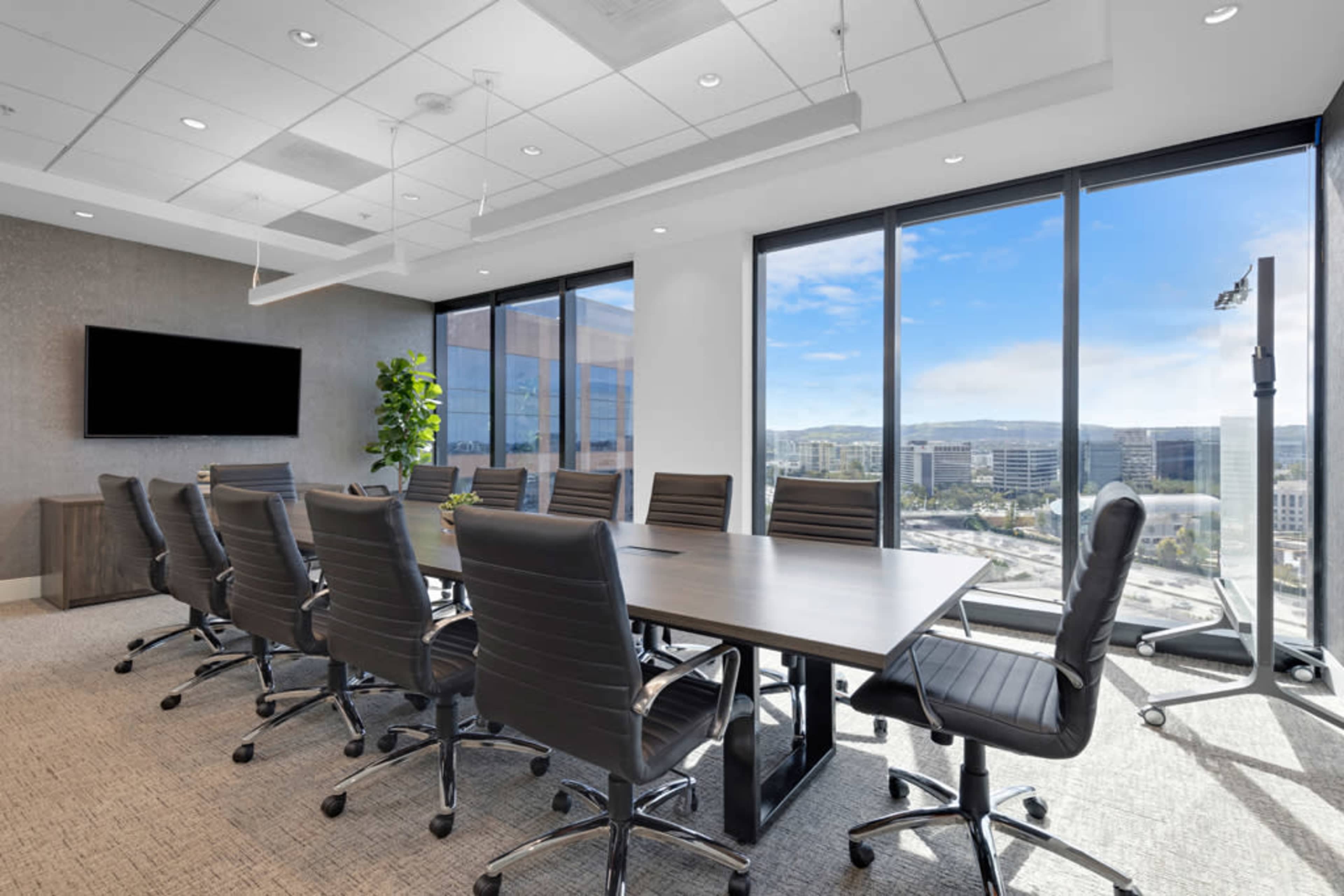 A modern conference room features a large table surrounded by ergonomic chairs, with large windows offering a view of the cityscape.