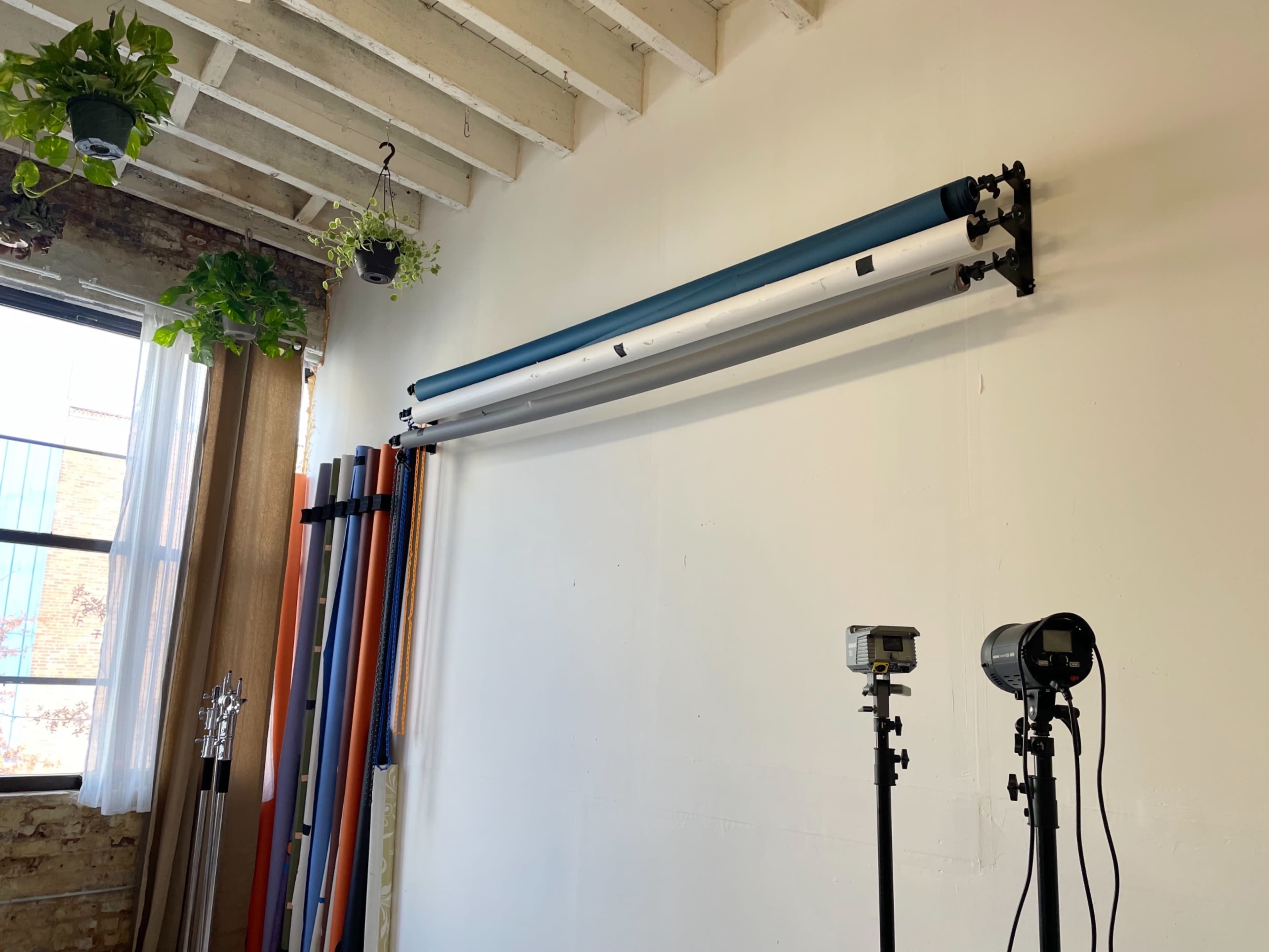 The image shows a studio wall with a mounted backdrop system and lighting equipment positioned nearby.