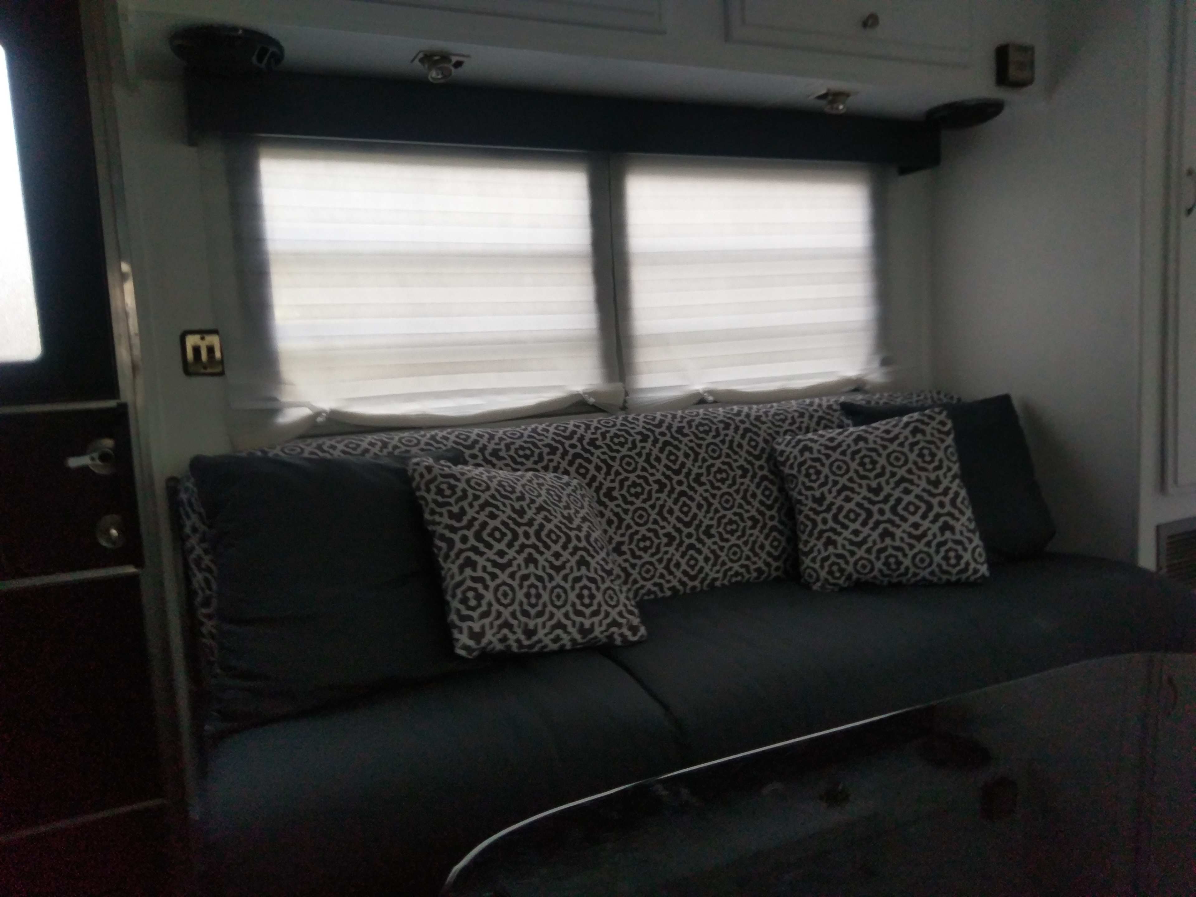 A cozy seating area with a dark, patterned sofa and several decorative pillows, positioned near two window shades.