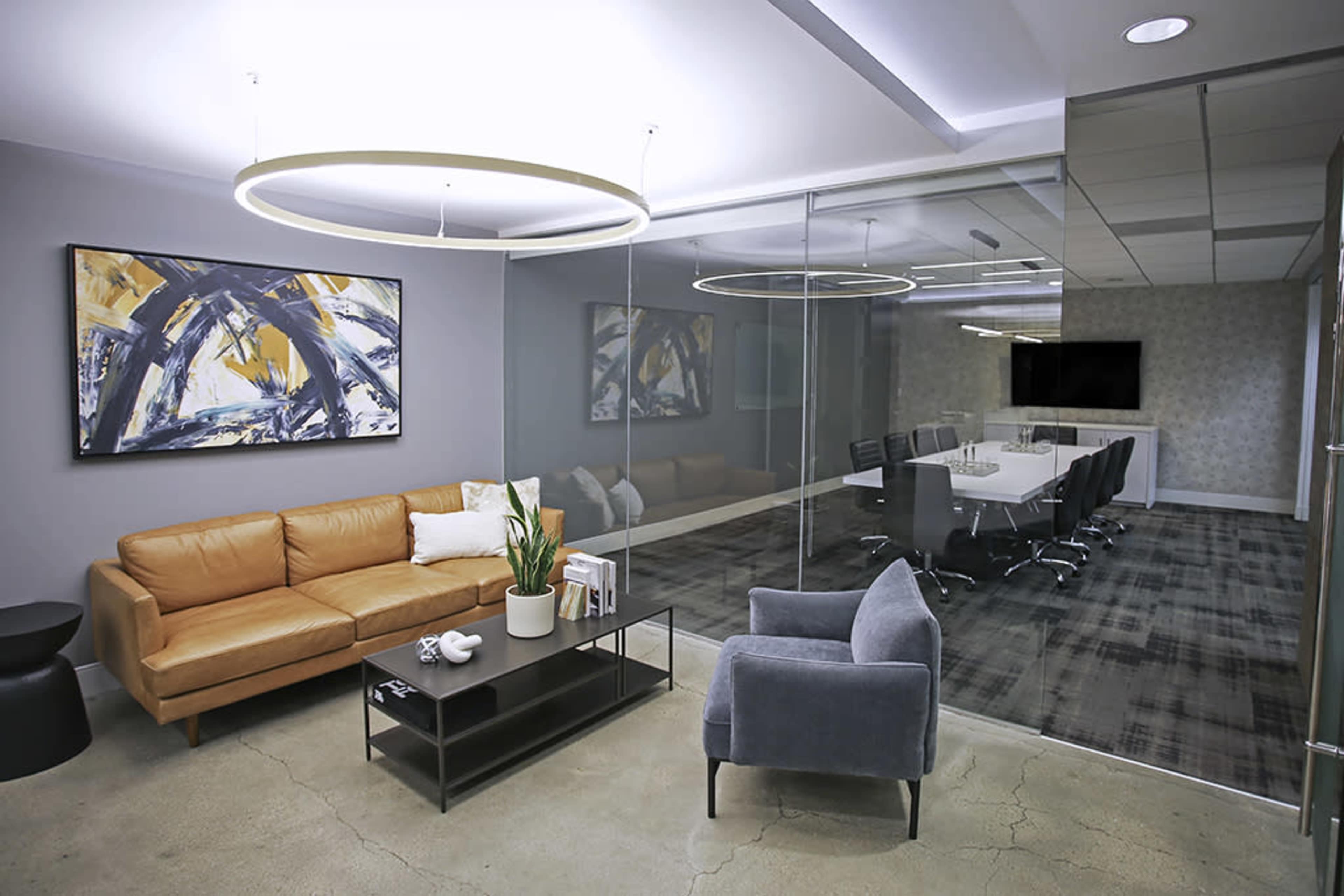 The image shows a modern office space featuring a leather sofa, a coffee table, and a glass-walled conference room with a large table and chairs.