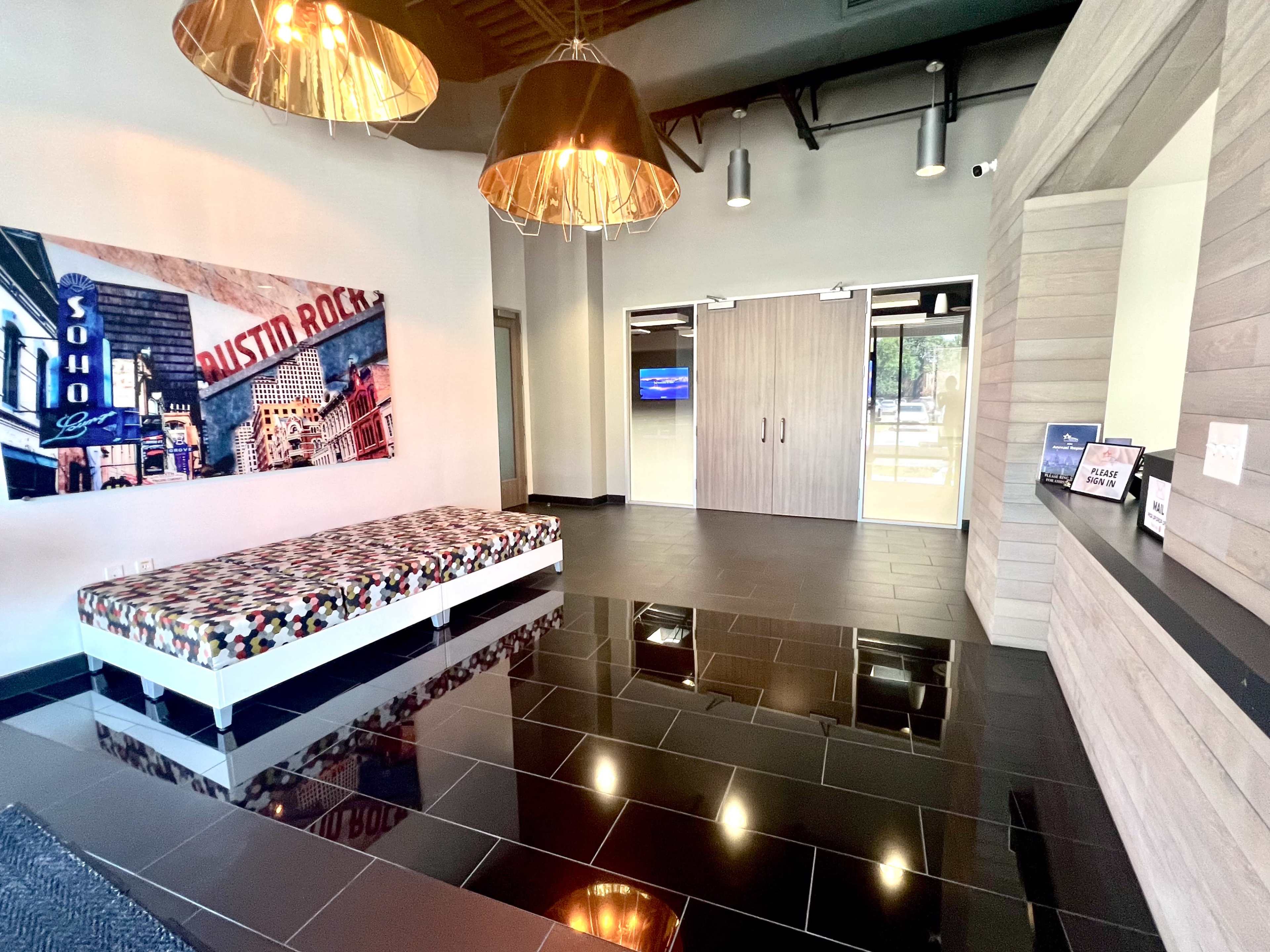 The image shows a modern lobby area featuring a patterned bench, pendant lighting, and a large wall mural of a cityscape.