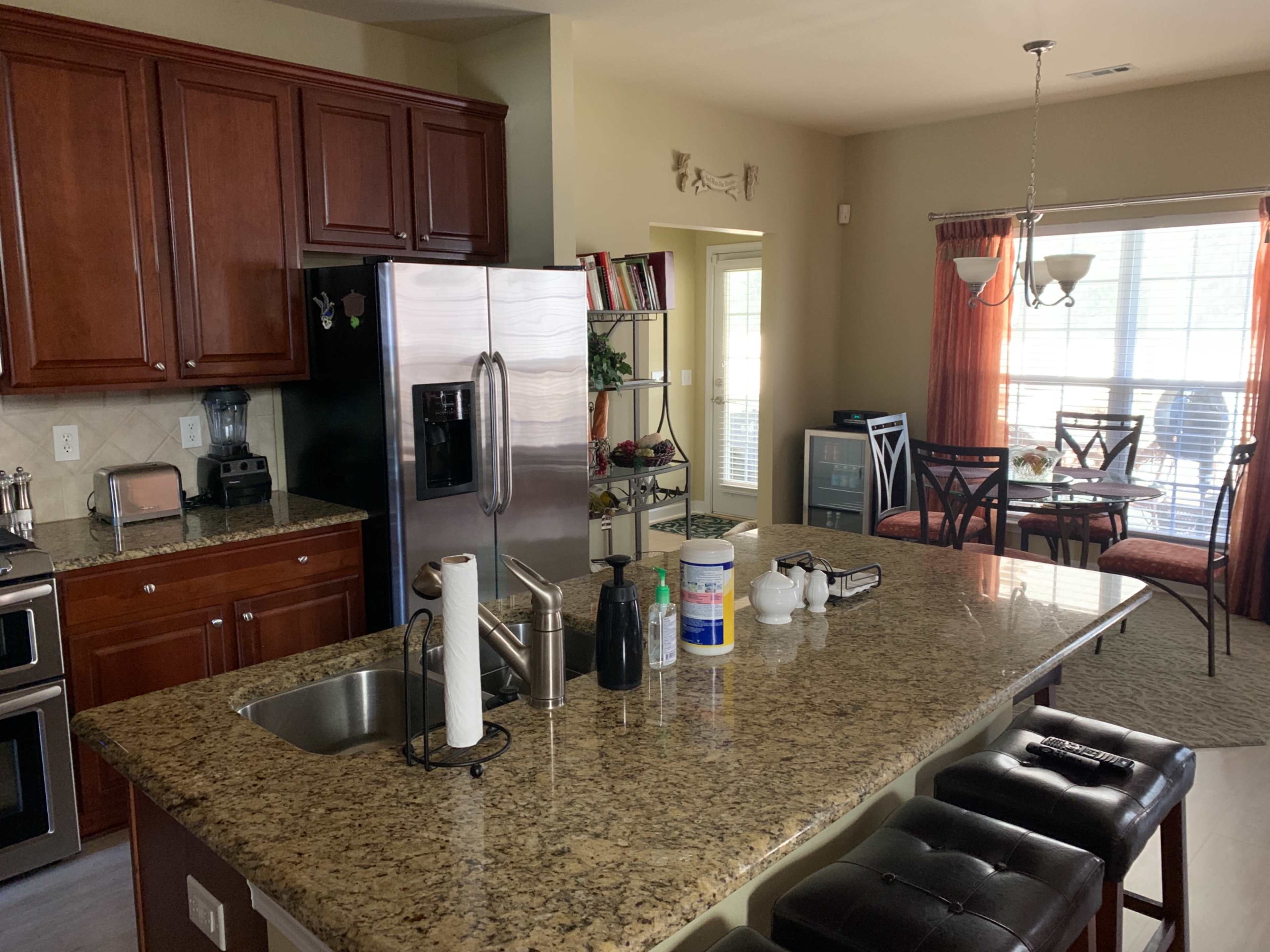 A kitchen with wooden cabinets, a granite countertop, and modern appliances, connected to a dining area with large windows.