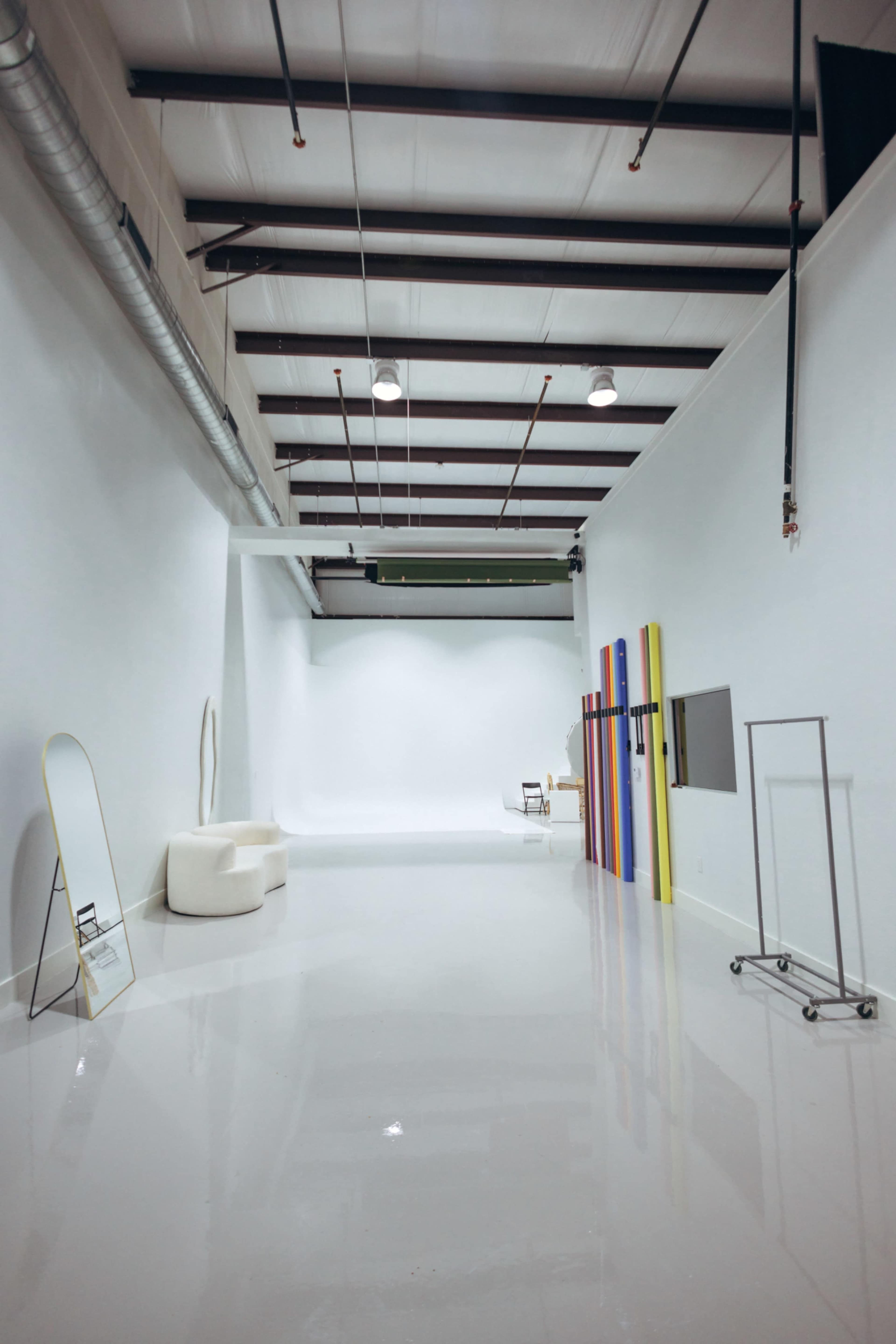 The image shows a spacious, well-lit studio with white walls, a polished floor, and colorful backdrops arranged along one side.
