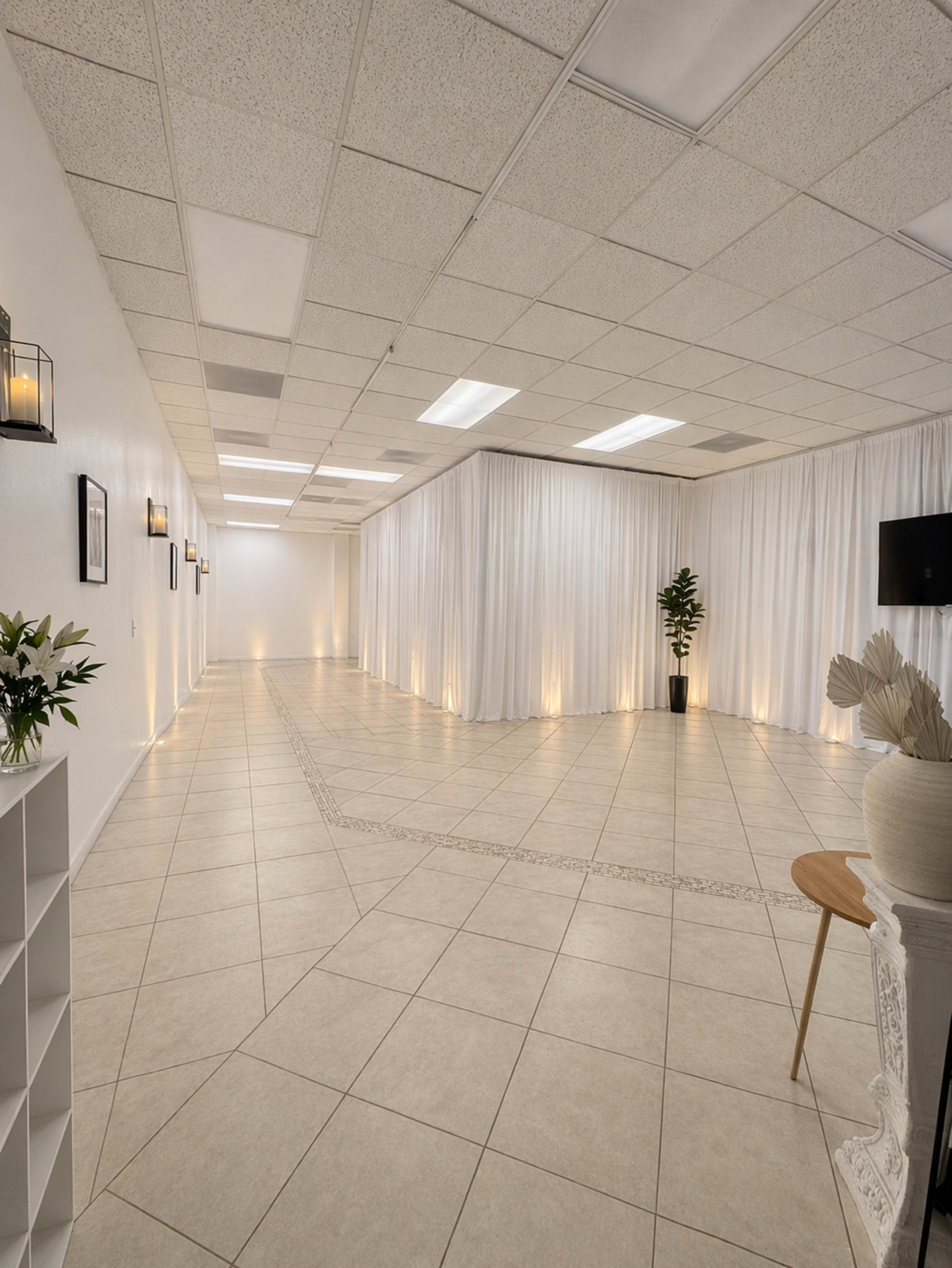 The image shows a spacious room with tiled flooring, white drapes along the walls, and several light fixtures casting soft illumination.