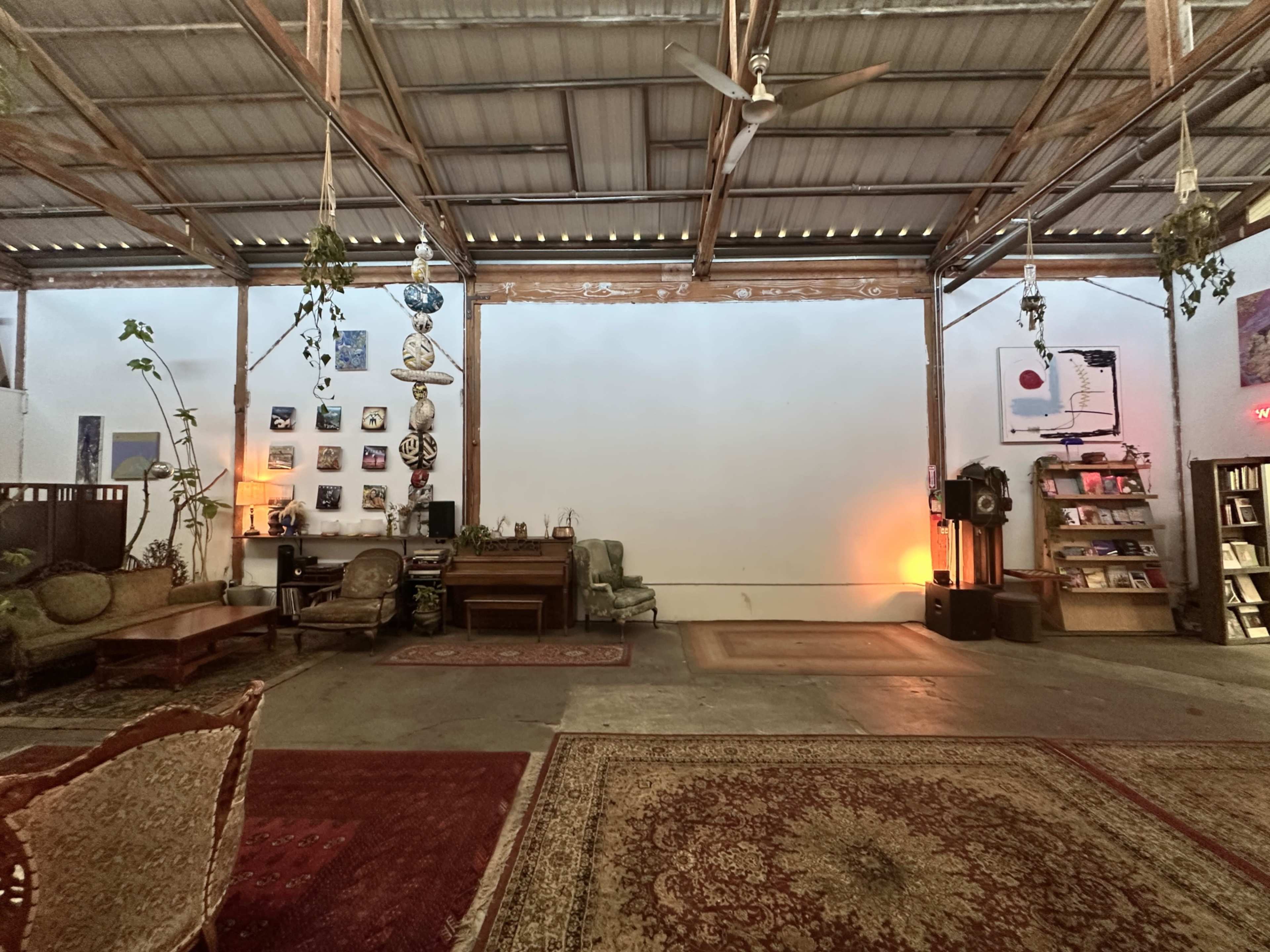 The image shows an open, spacious interior with wooden beams, decorated walls, and various furnishings including a sofa and a bookshelf.