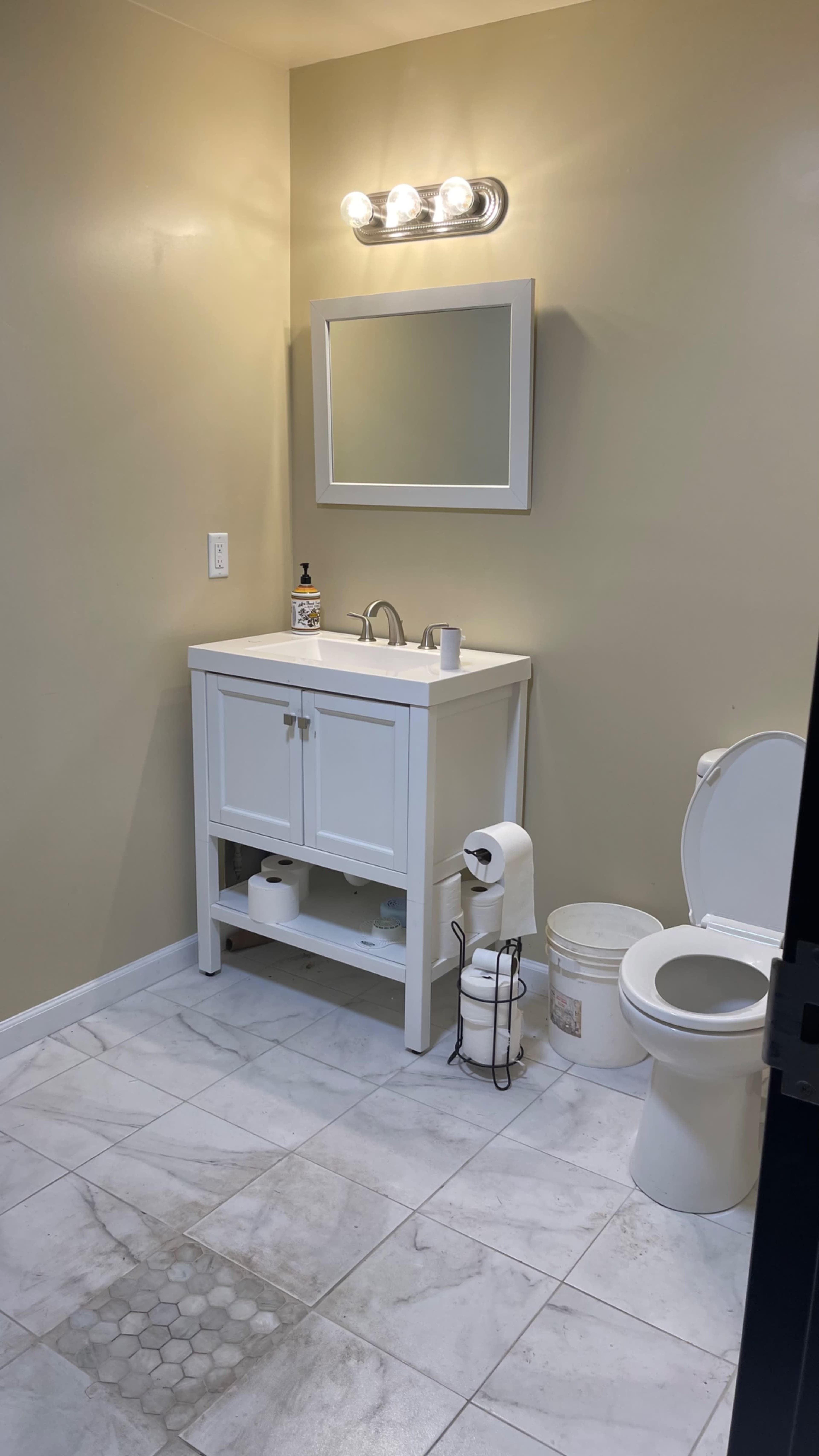 A small bathroom featuring a white vanity with a sink, a mirror above it, a toilet, and tiled flooring.
