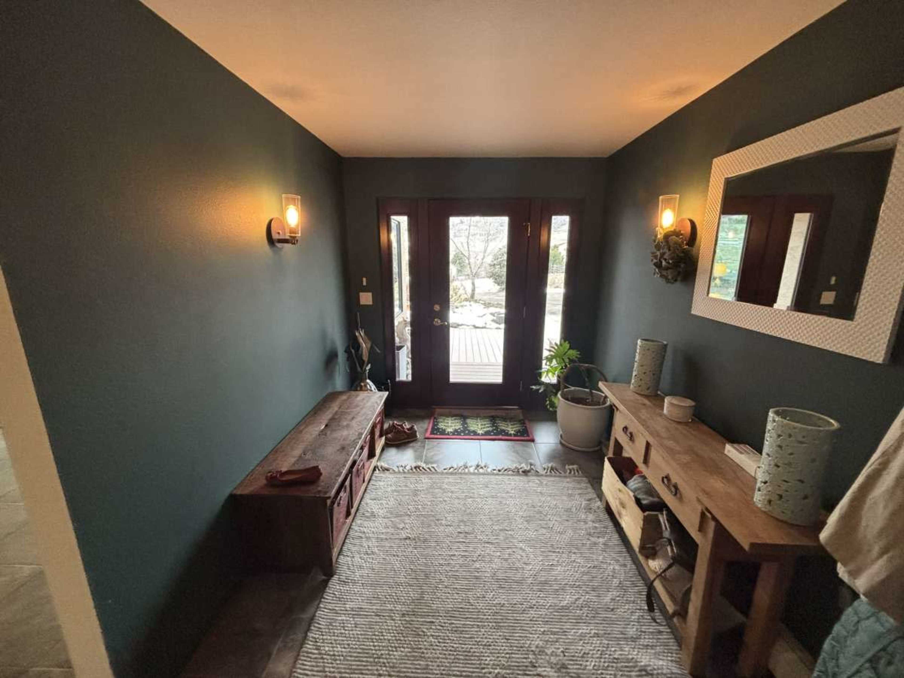 The image shows an entryway featuring a bench, a console table, and a large mirror, with double doors leading outside.
