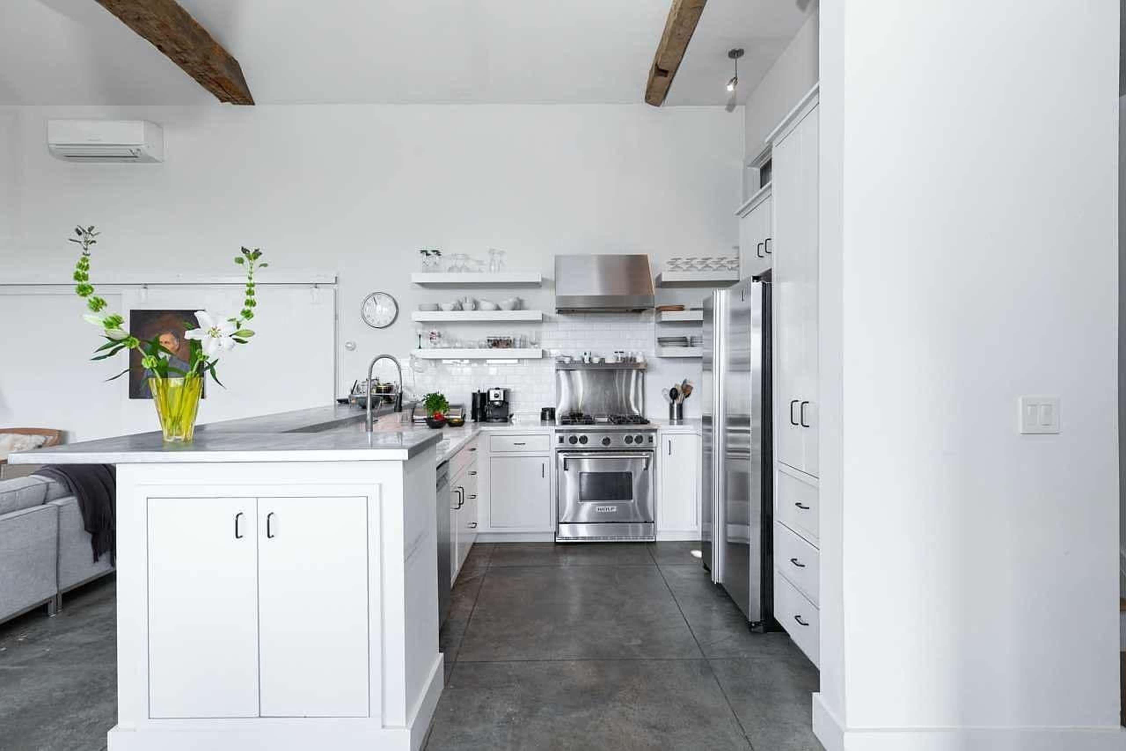 The image shows a modern kitchen featuring white cabinetry, stainless steel appliances, and a large island with a vase of flowers.