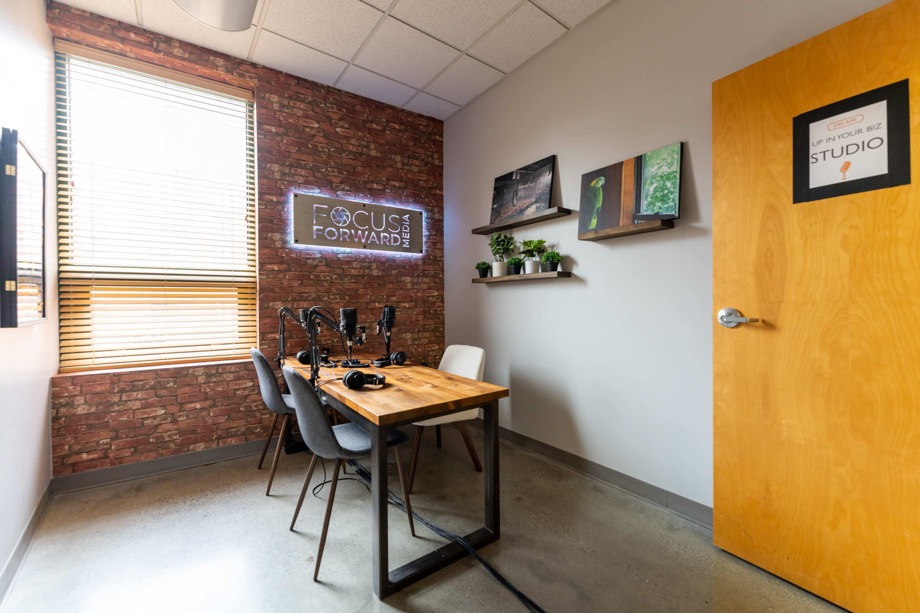 A small recording studio featuring a wooden table with microphones, chairs, a brick wall, and a door labeled "STUDIO."