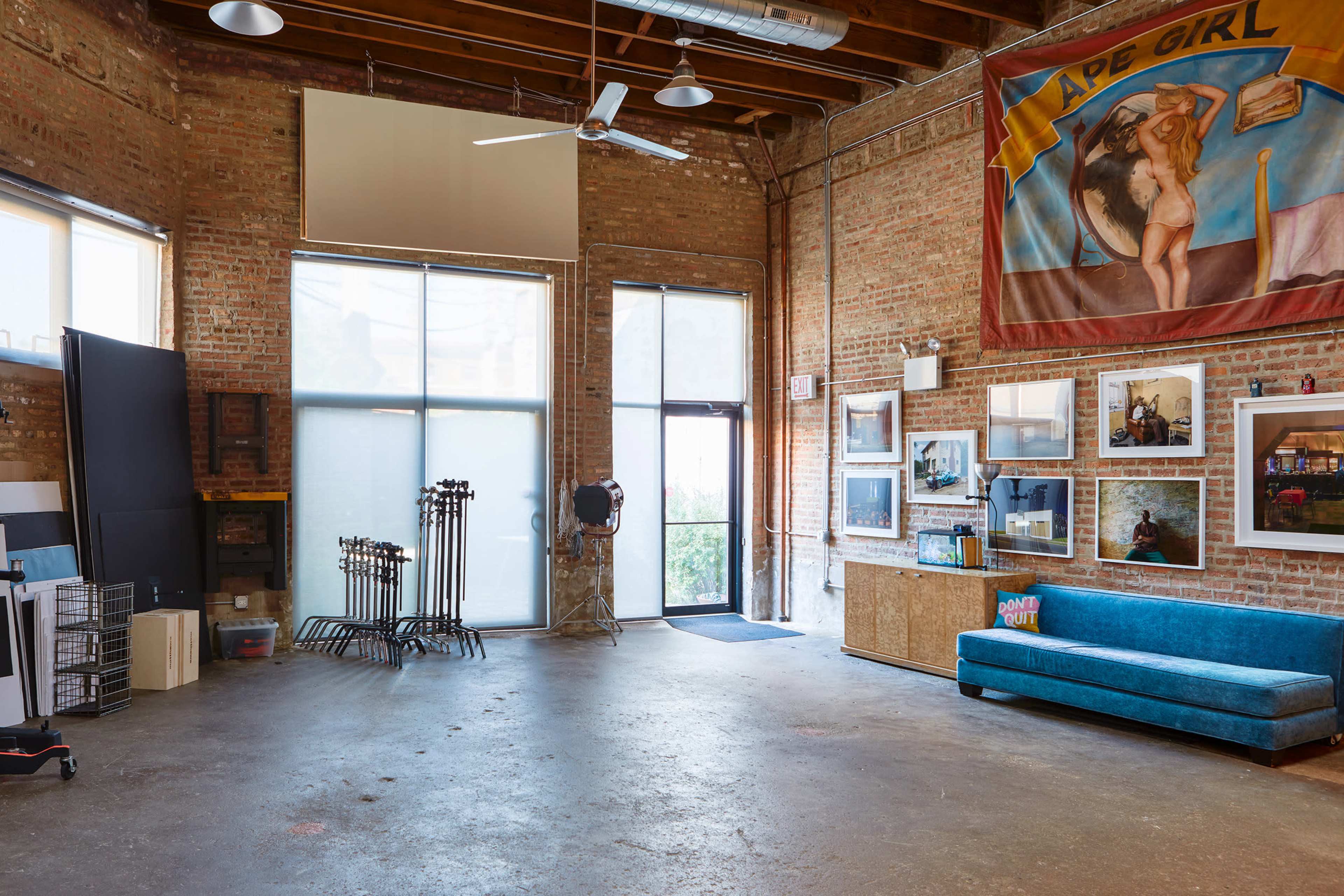 A spacious studio with exposed brick walls, large windows, and various artworks displayed on the walls, including a large banner.