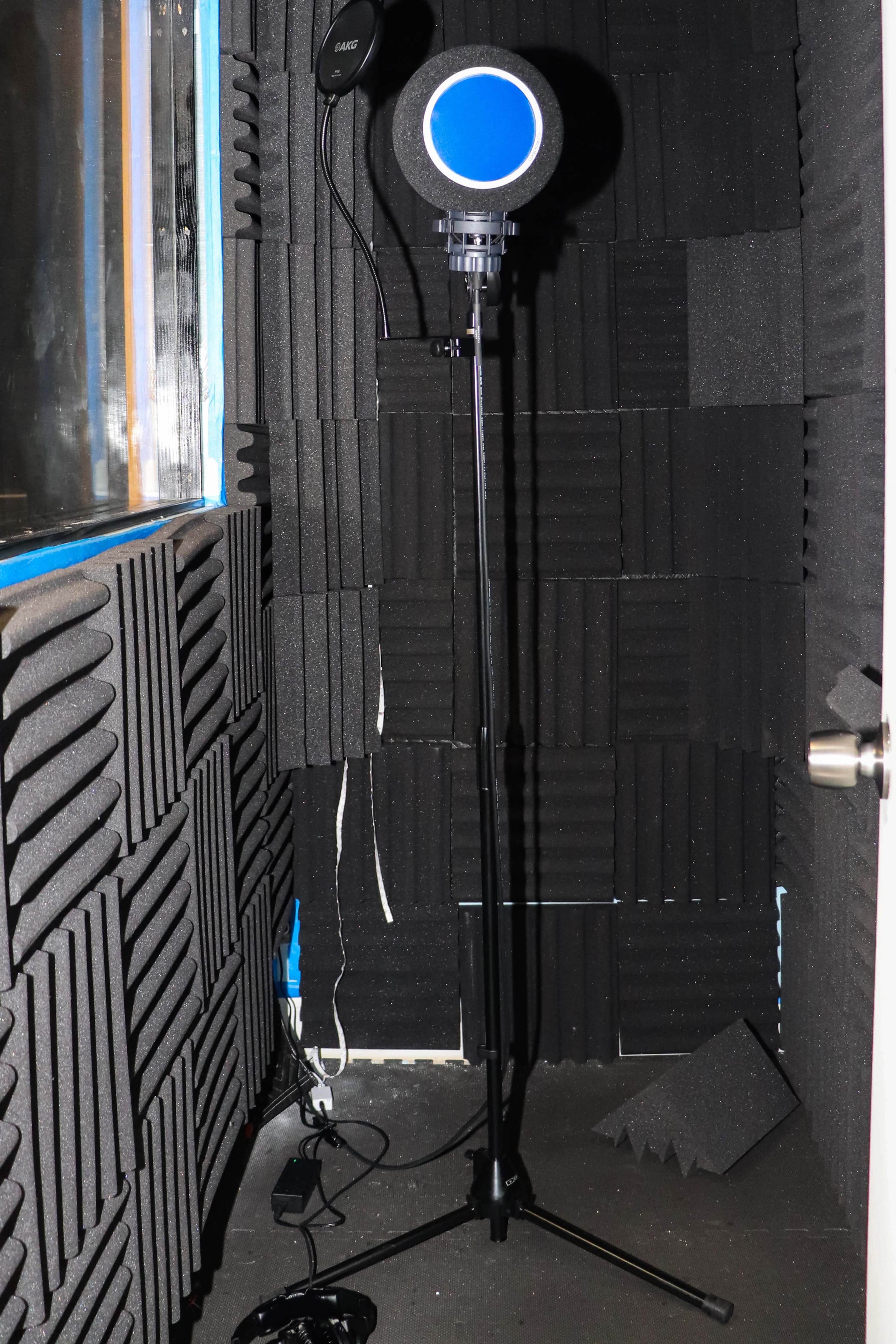 The image shows a soundproof booth lined with acoustic panels and a microphone on a stand in the corner.