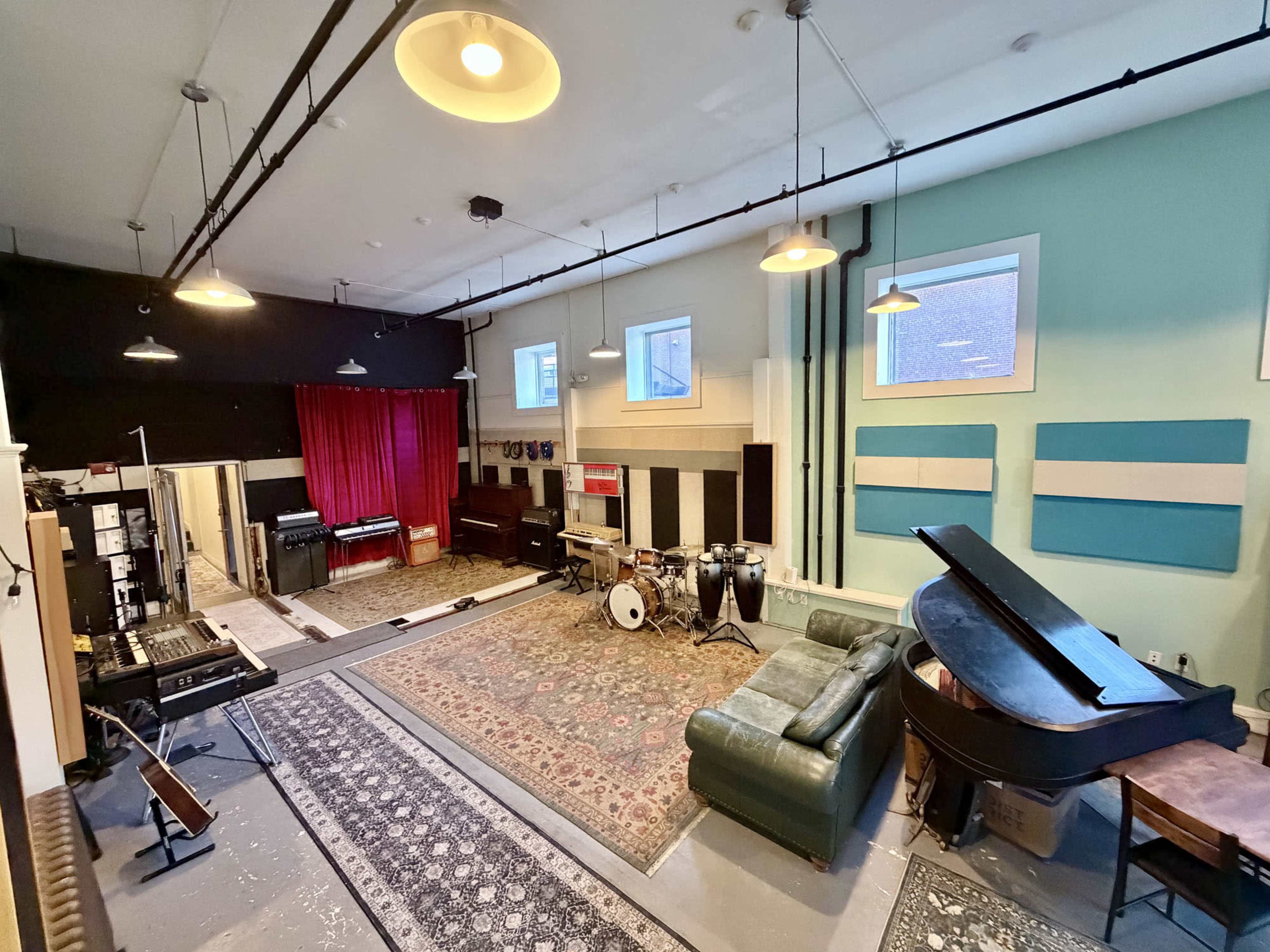A spacious music studio features a variety of instruments, including a drum set and a grand piano, along with area rugs and colorful wall panels.