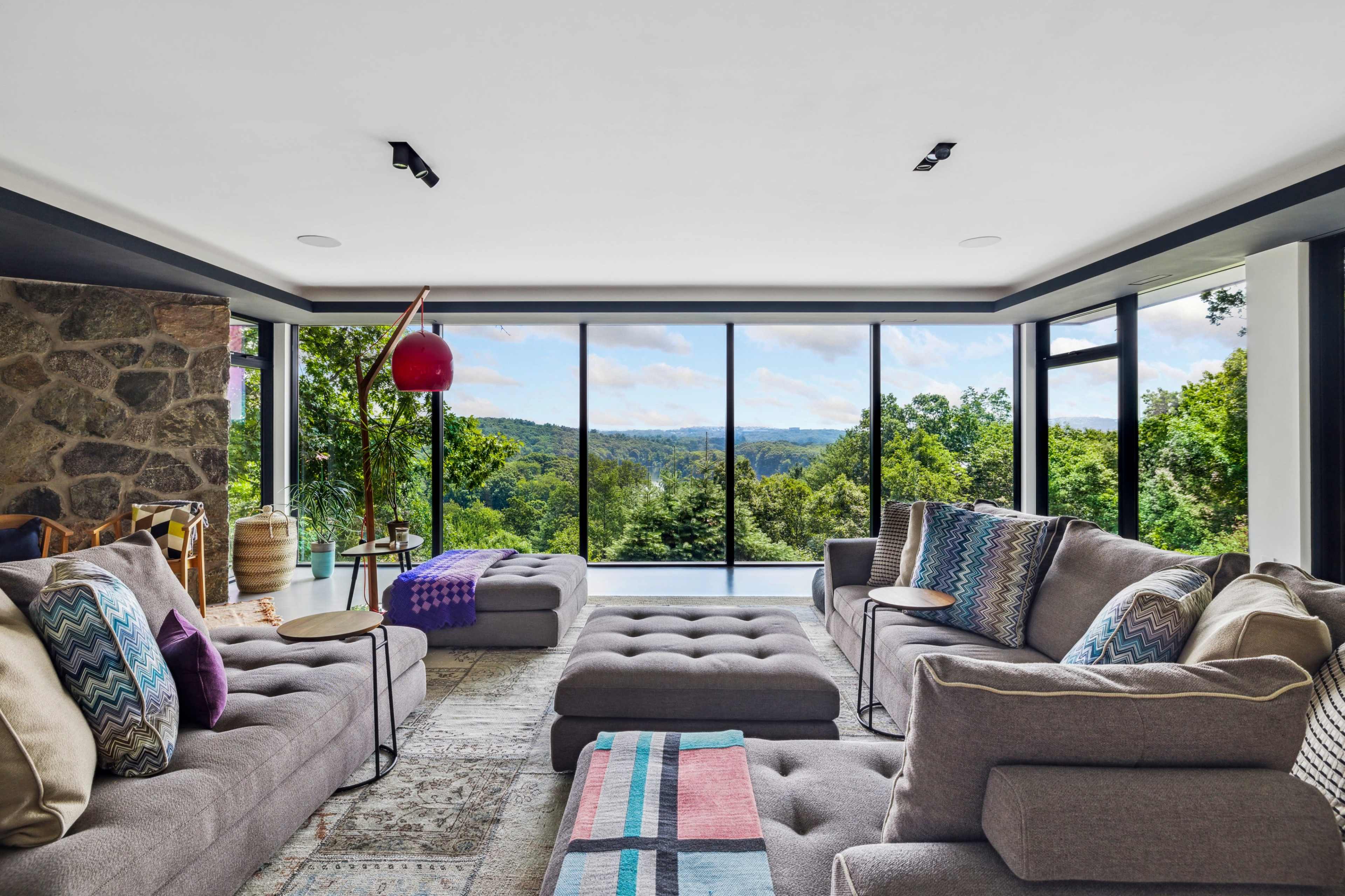 A modern living room features large windows with expansive views of green hills, showcasing comfortable gray sofas adorned with patterned cushions and a cozy throw.