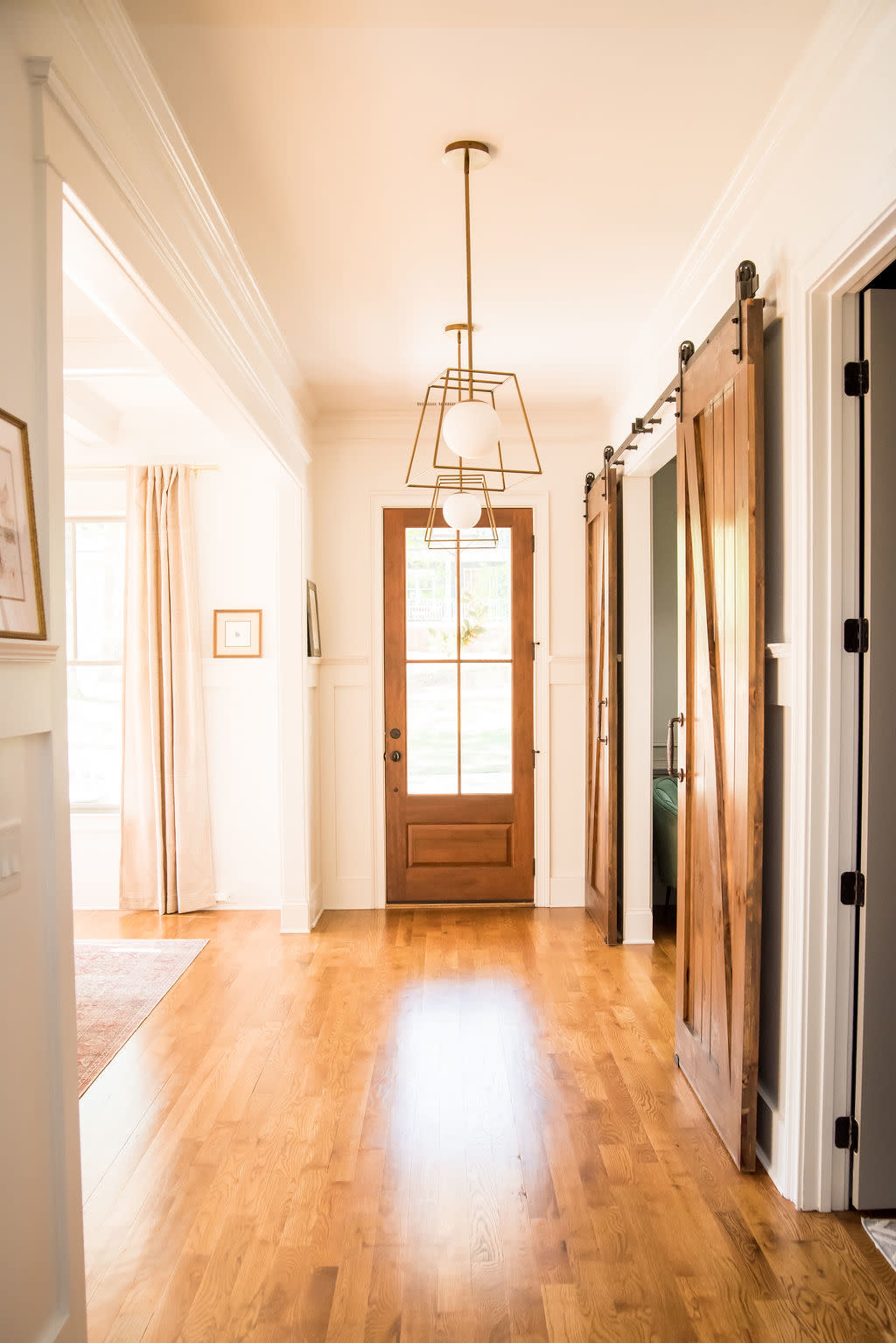A brightly lit hallway with wooden floors, featuring a wooden front door and two sliding barn doors on either side.