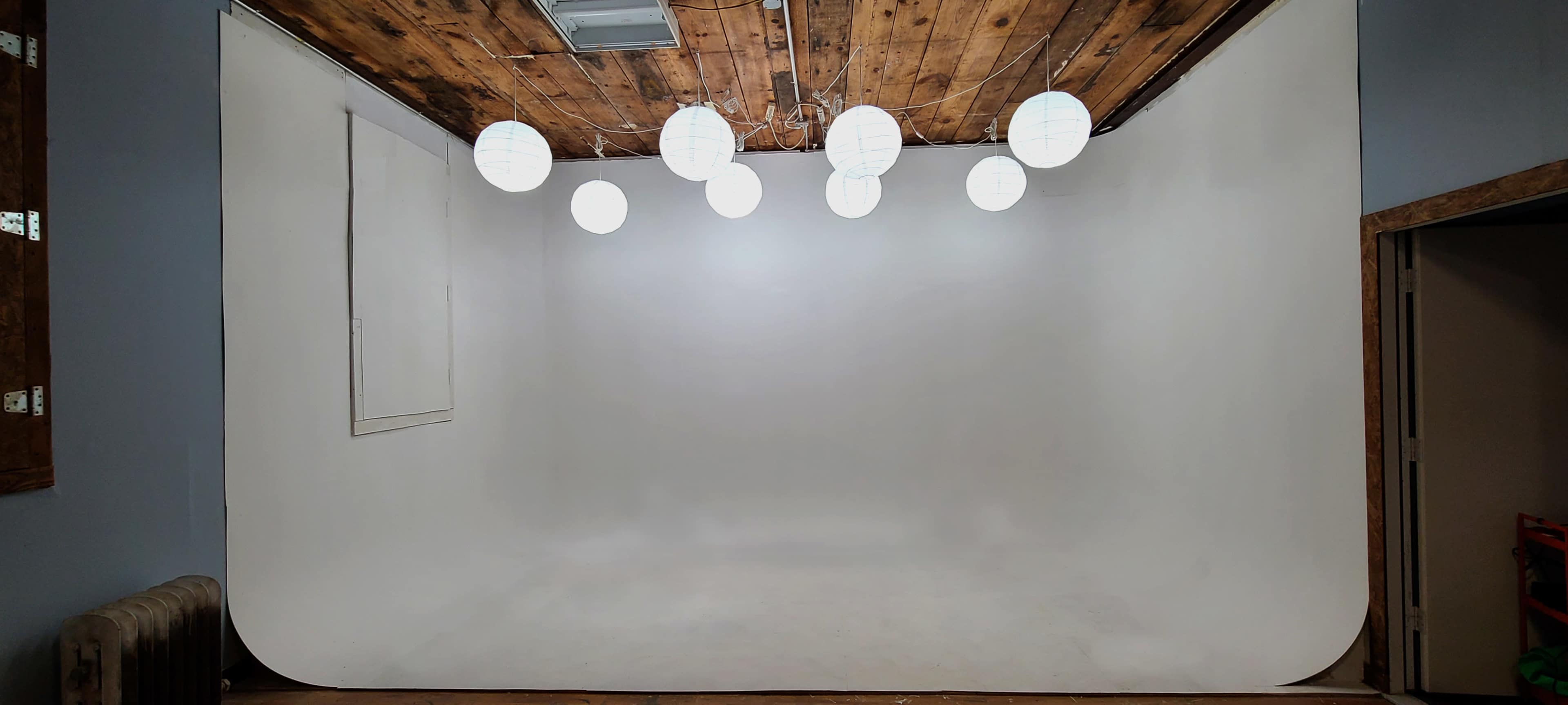 The image shows a spacious, well-lit studio with a white backdrop and several round paper lanterns suspended from the ceiling.