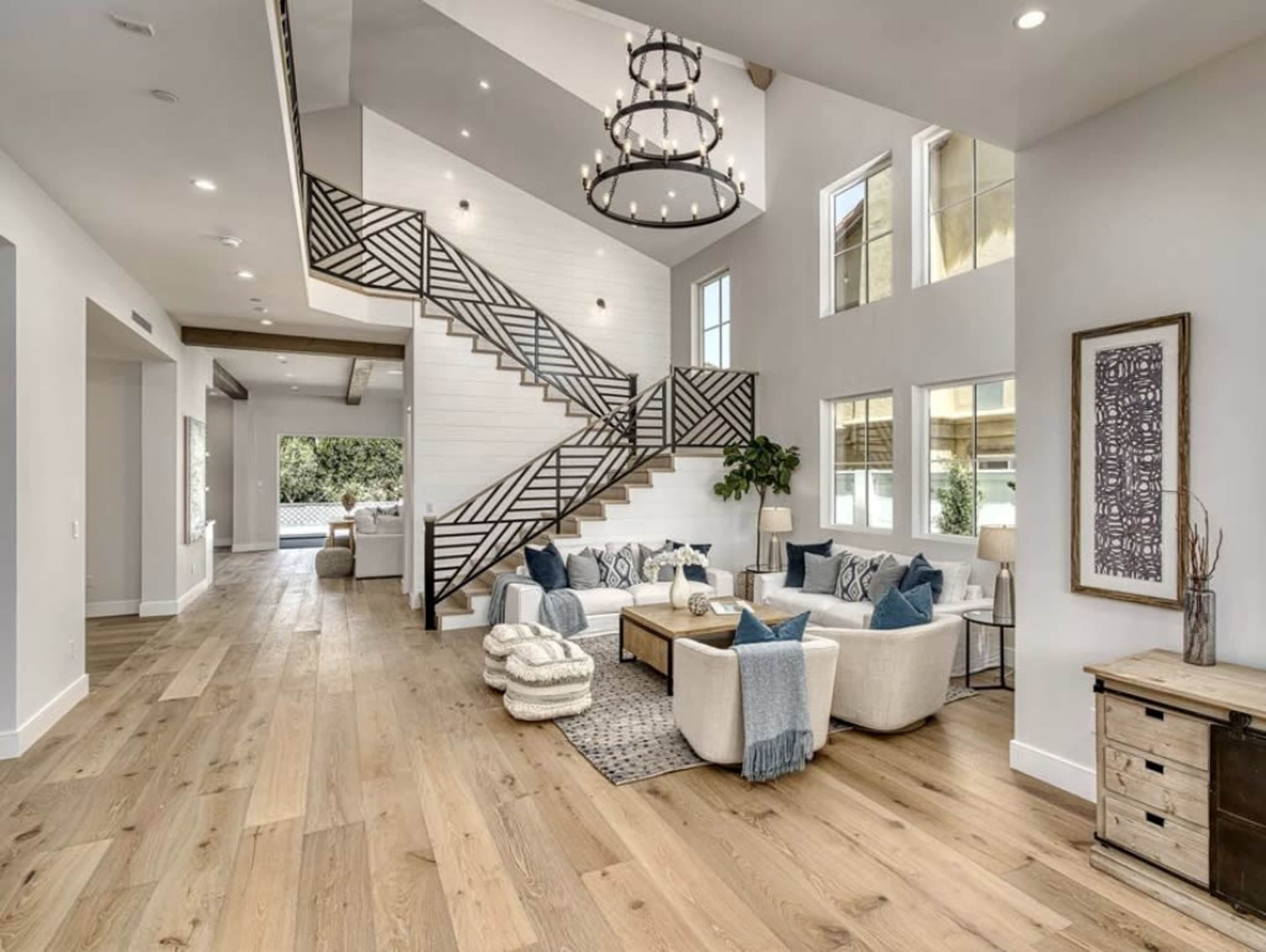 A modern living room featuring a staircase with a patterned railing, a large area rug, and several seating arrangements with throw pillows.