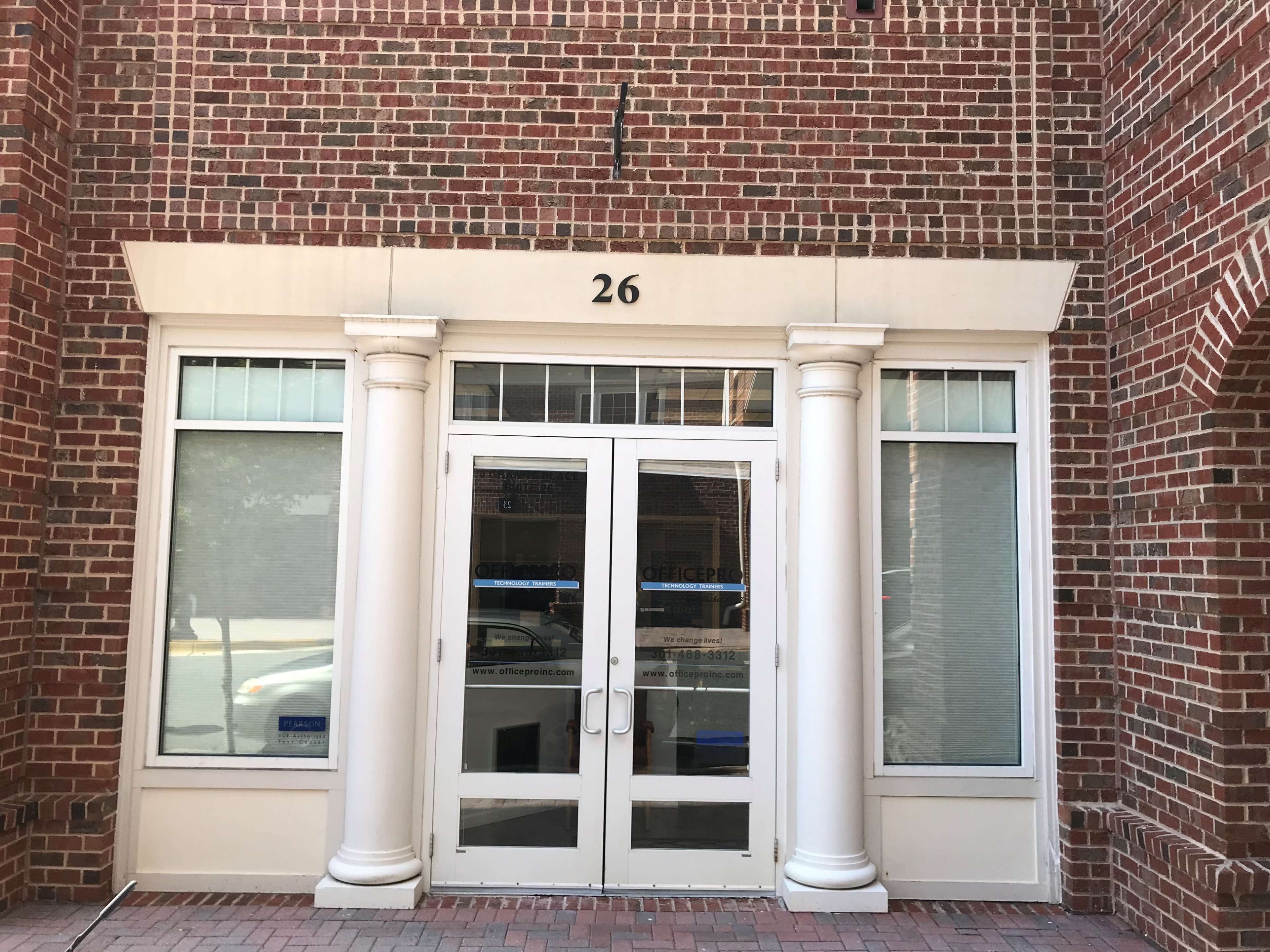 The entrance of a building with a large double door, flanked by two white columns, marked with the number 26 above.