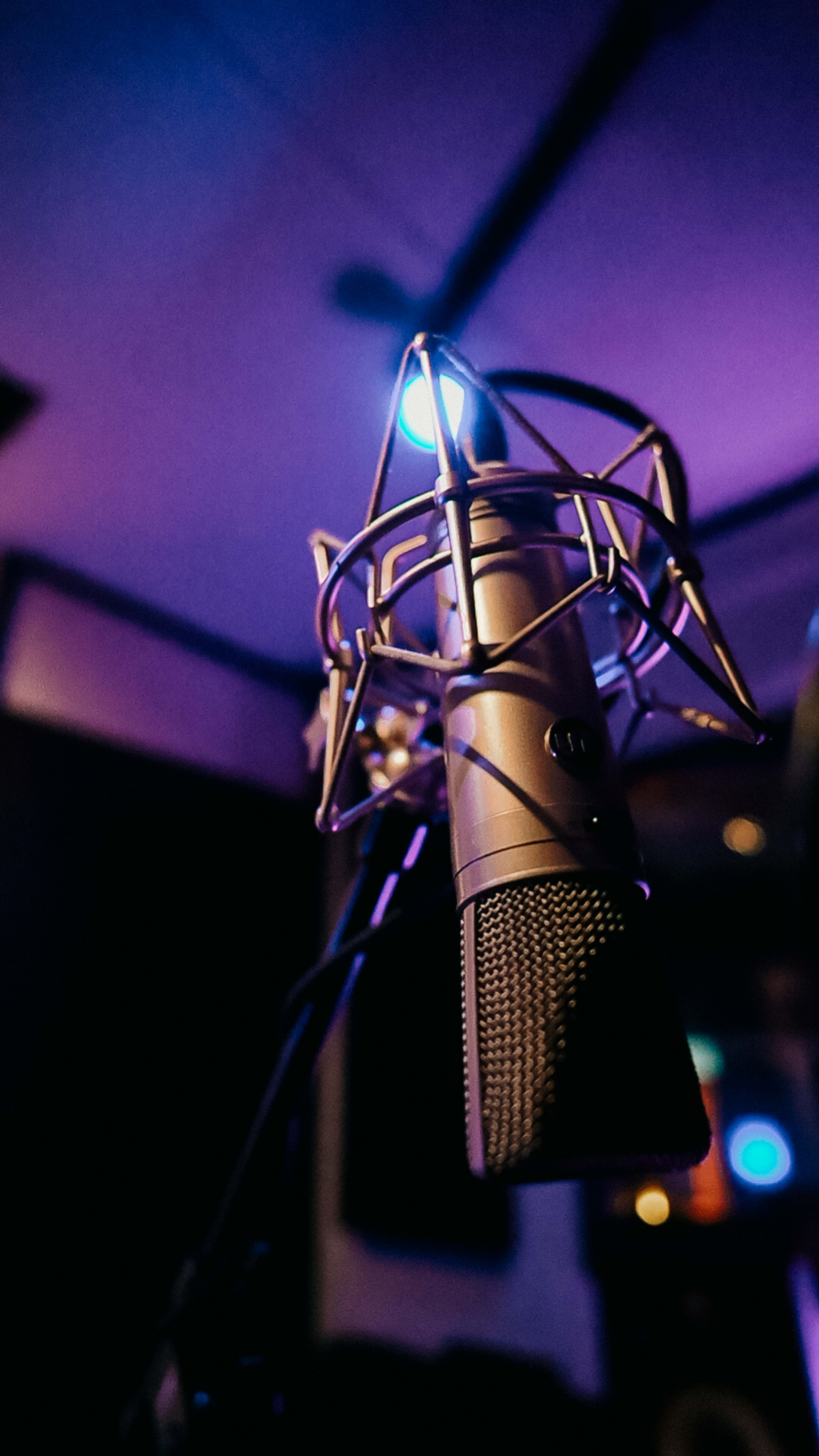 A close-up of a microphone in a dimly lit recording studio, surrounded by soft purple lighting.