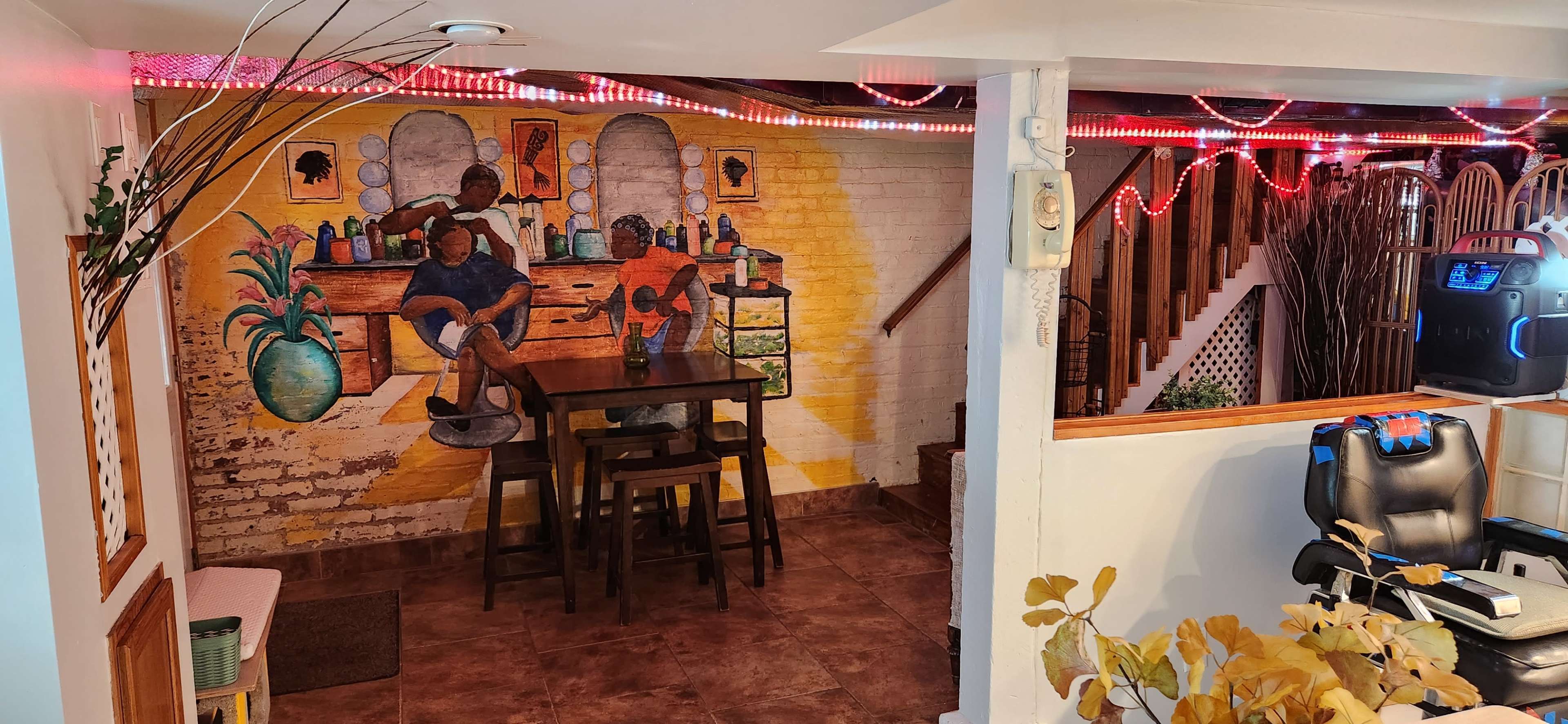 A basement interior featuring a mural of two people at a countertop, a wooden table with chairs, and decorative lighting along the ceiling.