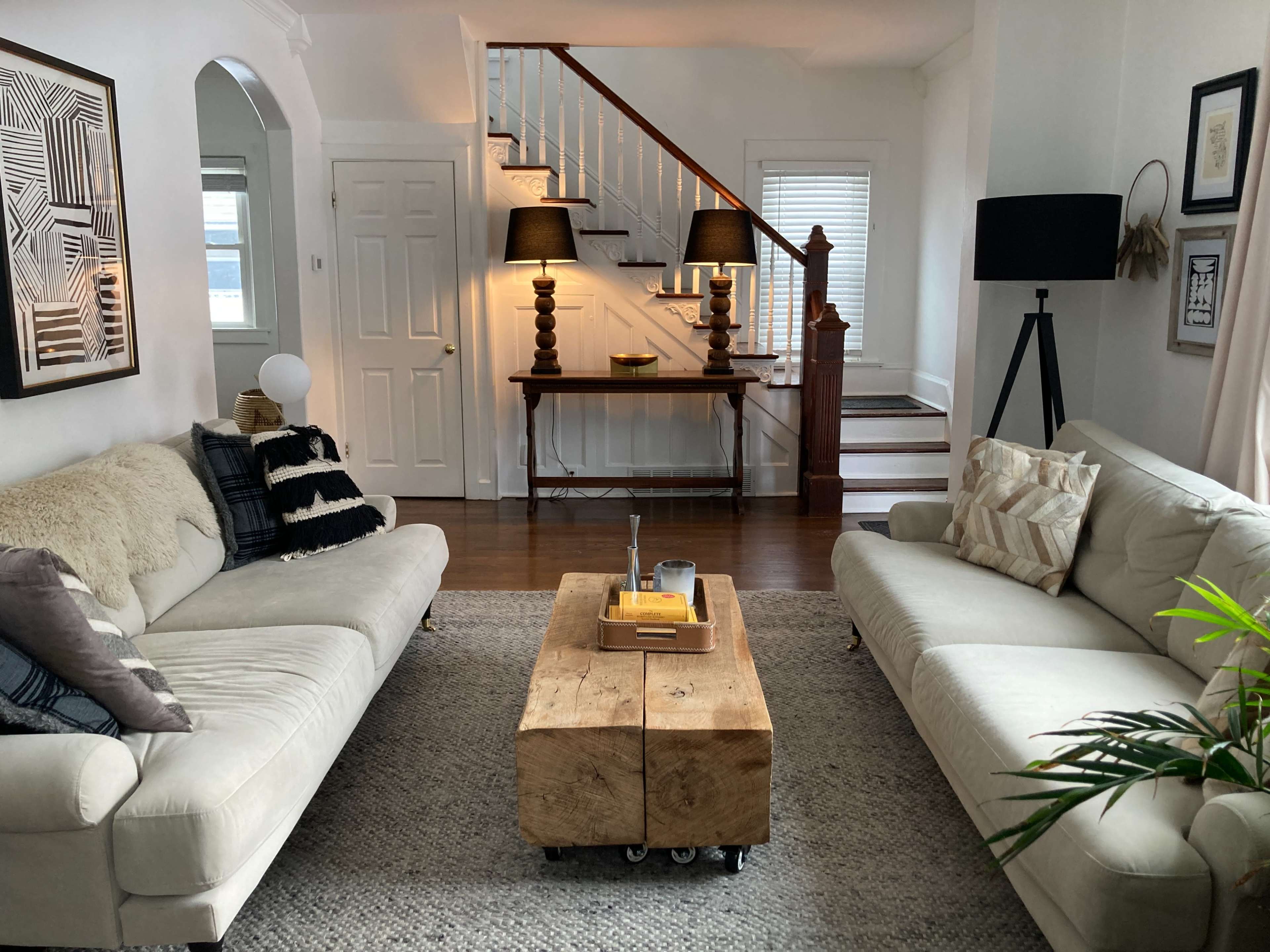 A living room with two sofas facing each other, a central wooden coffee table on wheels, and a staircase in the background.