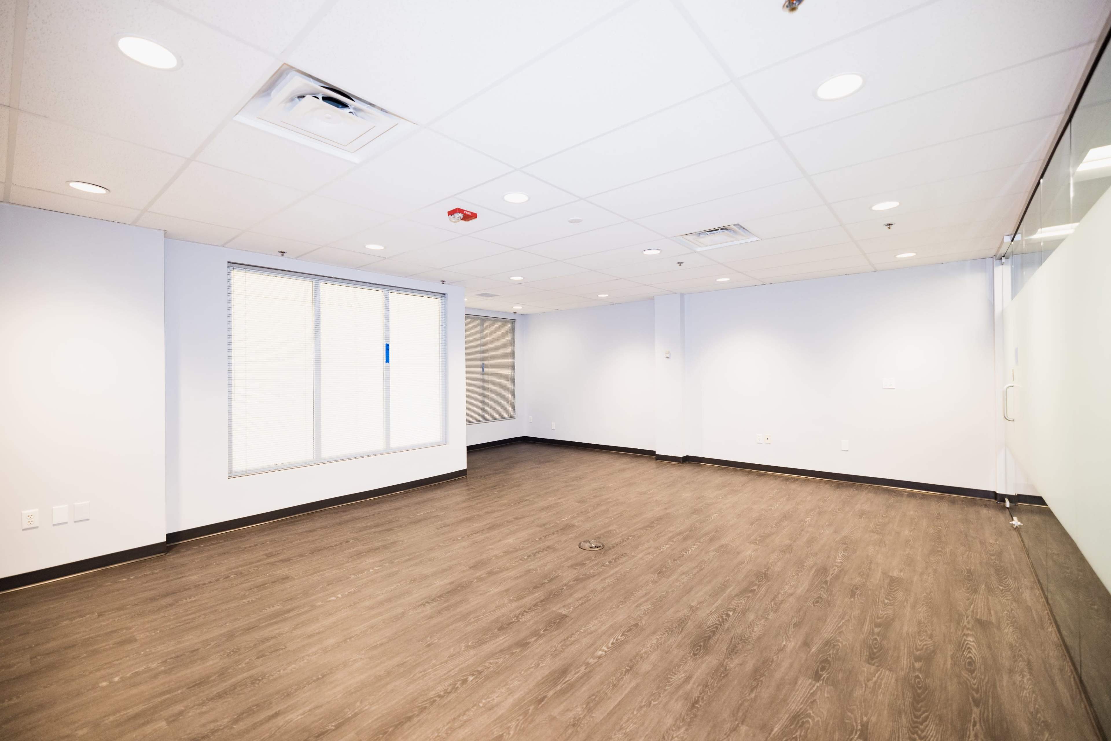 An empty office space features a light-colored floor, white walls, and a large window.