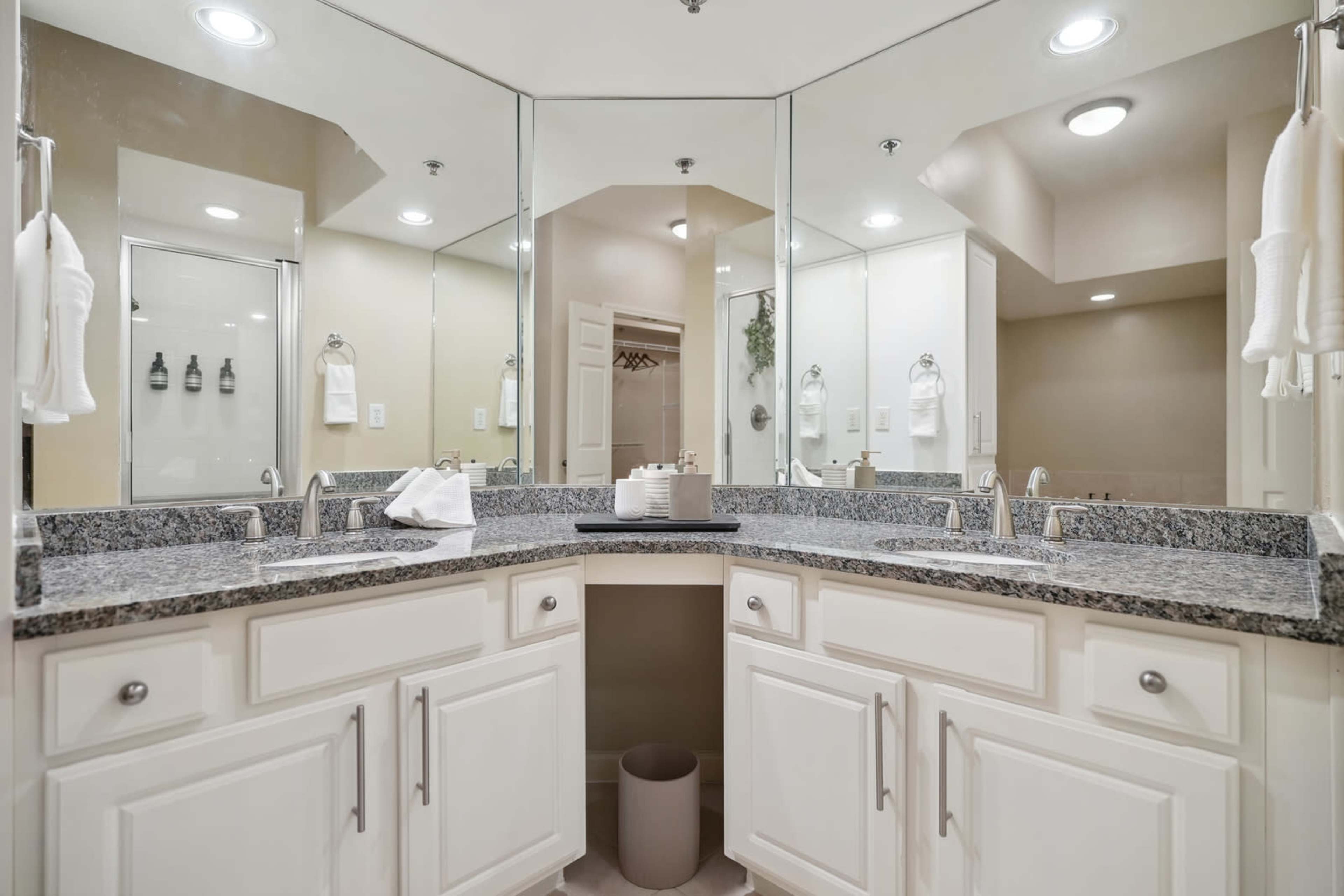 A spacious bathroom with a dual sink vanity, granite countertops, and large mirrors reflecting the space.