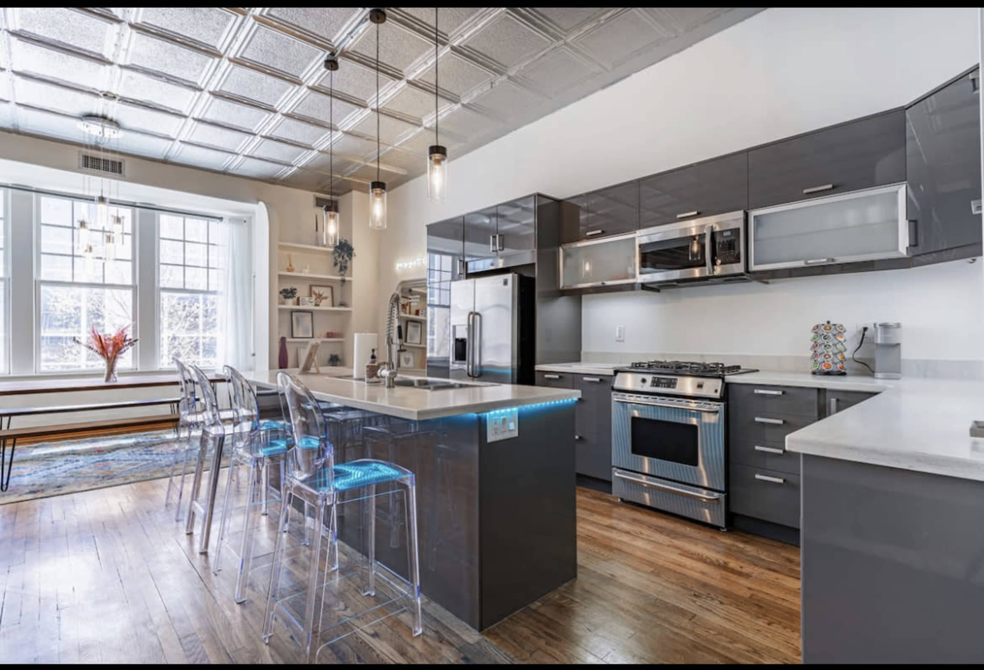 A modern kitchen with polished cabinetry, stainless steel appliances, and illuminated bar stools.