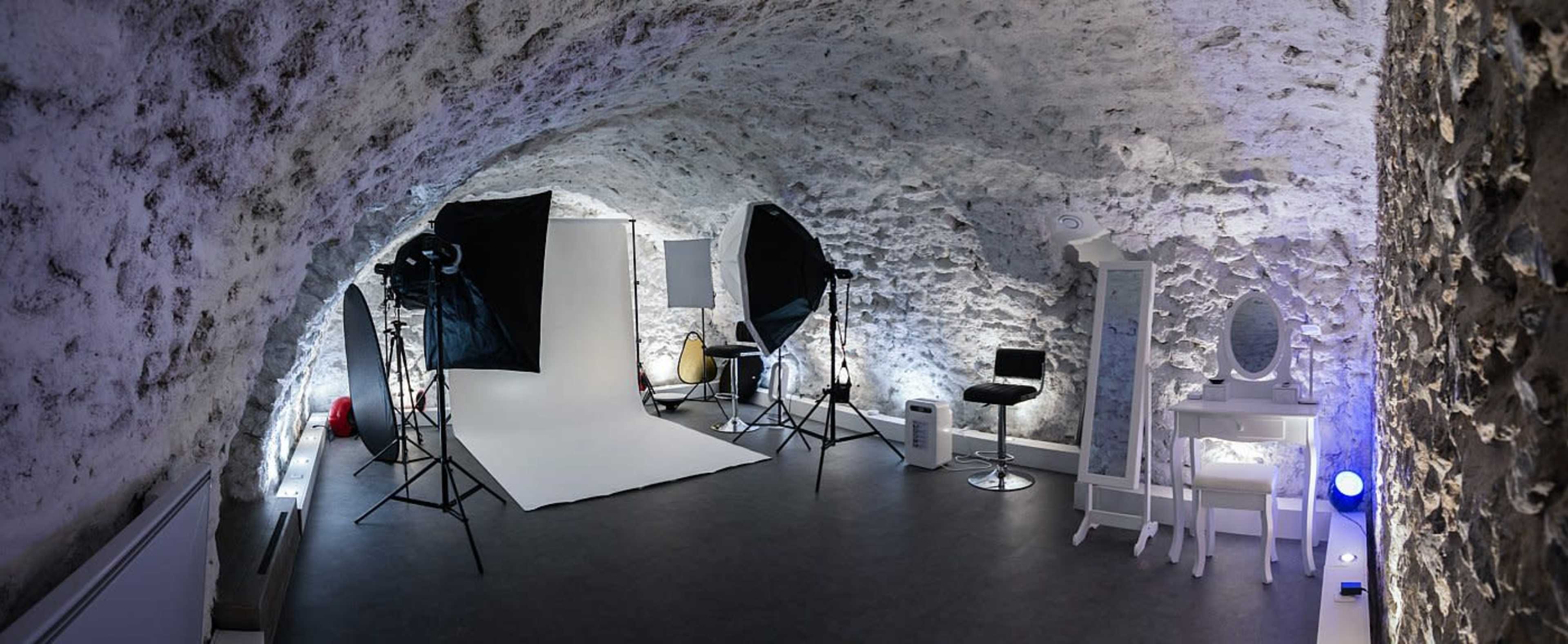 A photography studio with a white backdrop, lighting equipment, and various props in a stone-walled room.