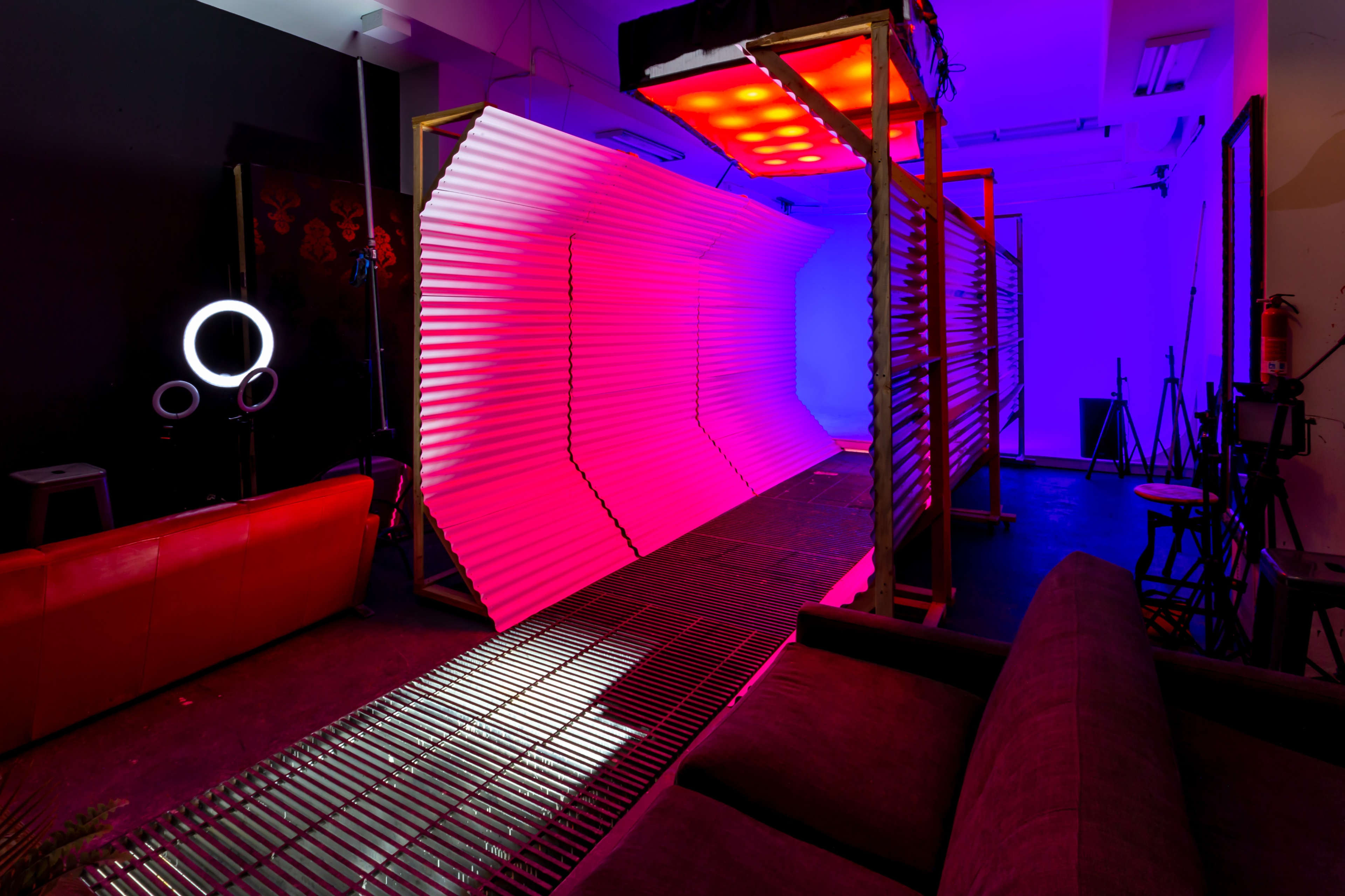 A studio space featuring a brightly lit, curved backdrop with colored lighting and seating areas in a contemporary design.
