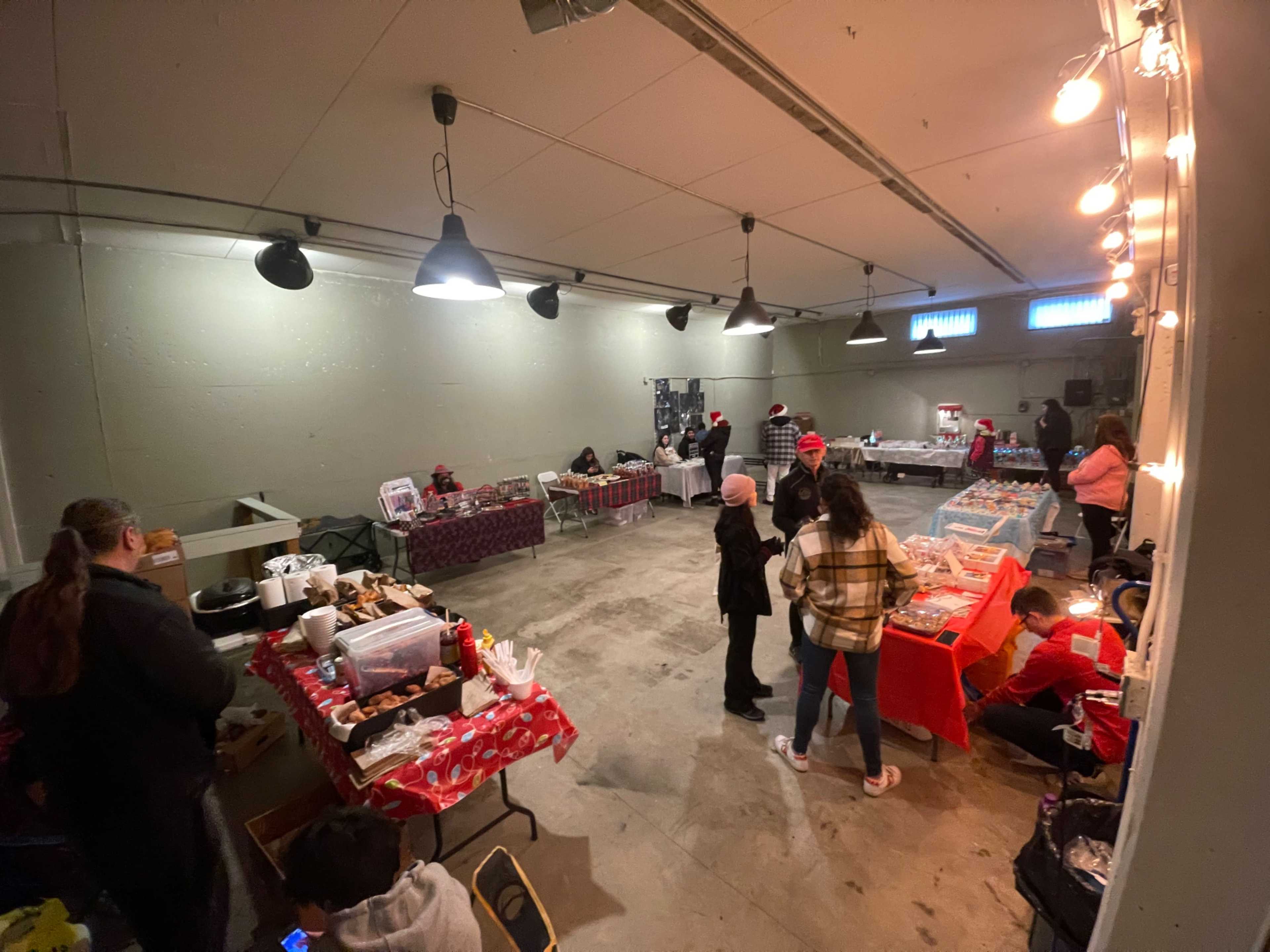 The scene shows a spacious indoor market with tables displaying various food items and people engaging with each other.