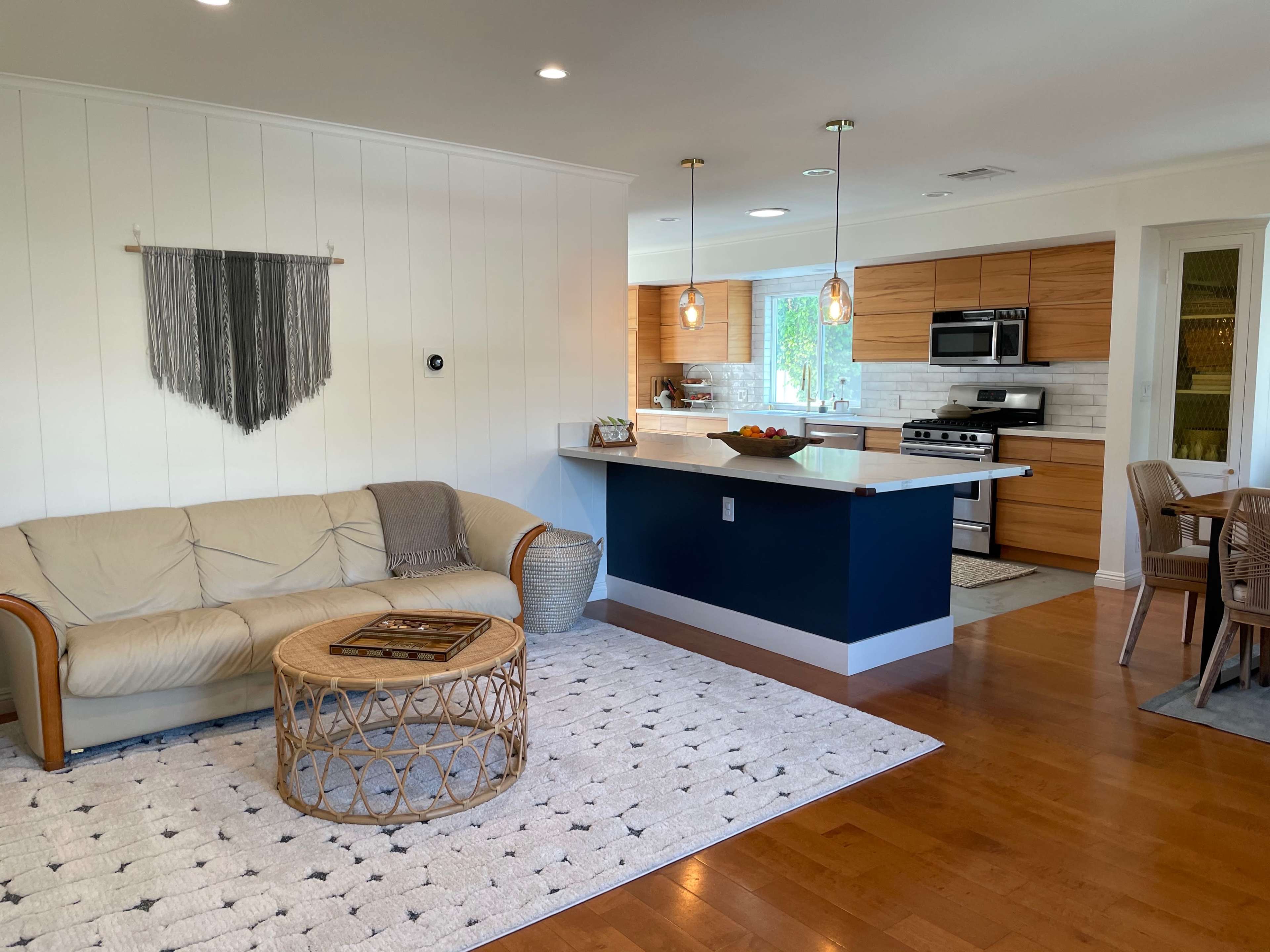 A modern living area features a light-colored sofa, a round woven coffee table, and an open kitchen with wooden cabinetry.