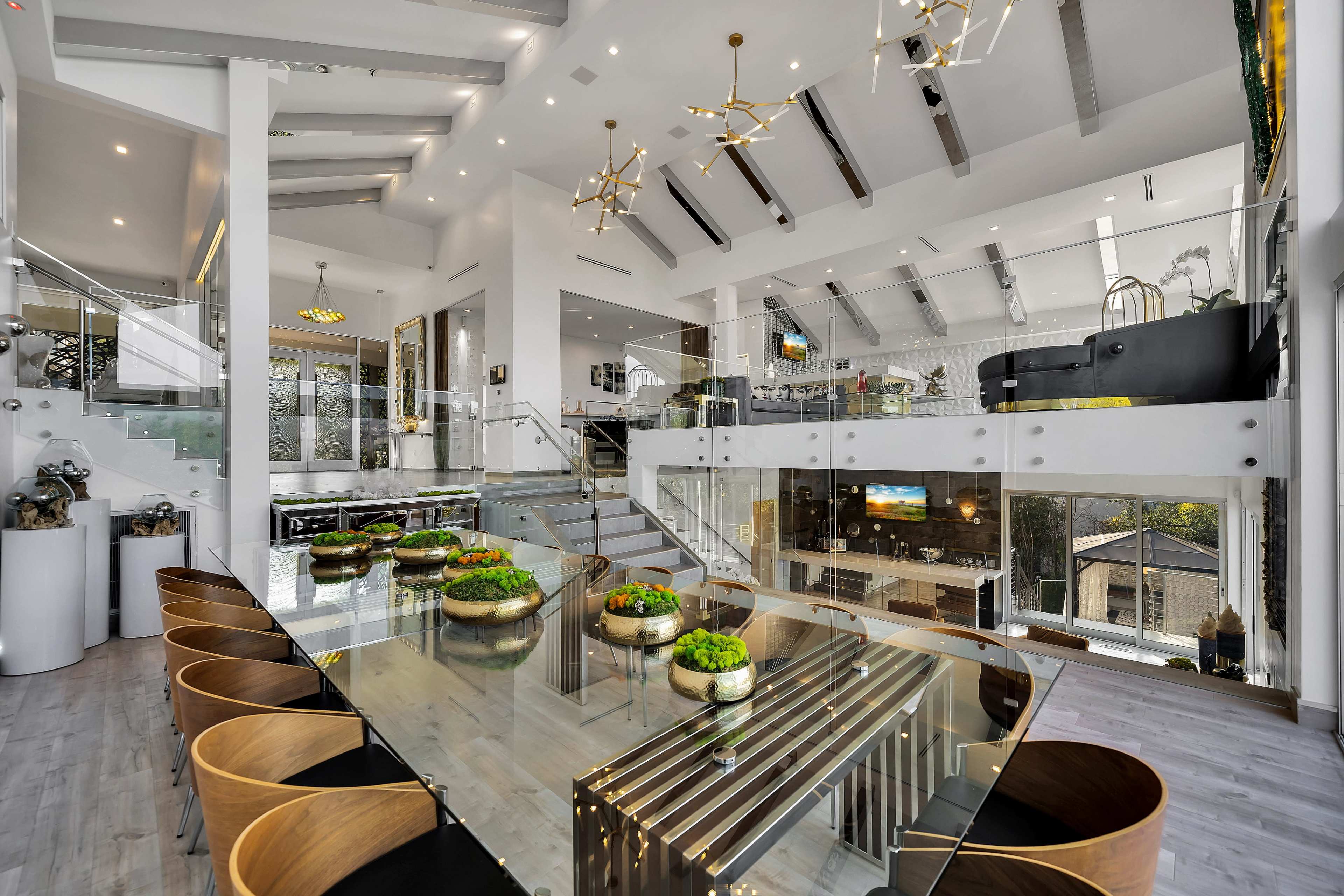 A modern, spacious dining area with a glass-top table surrounded by wooden chairs, featuring an open layout that connects to a stylish living area with contemporary decor.