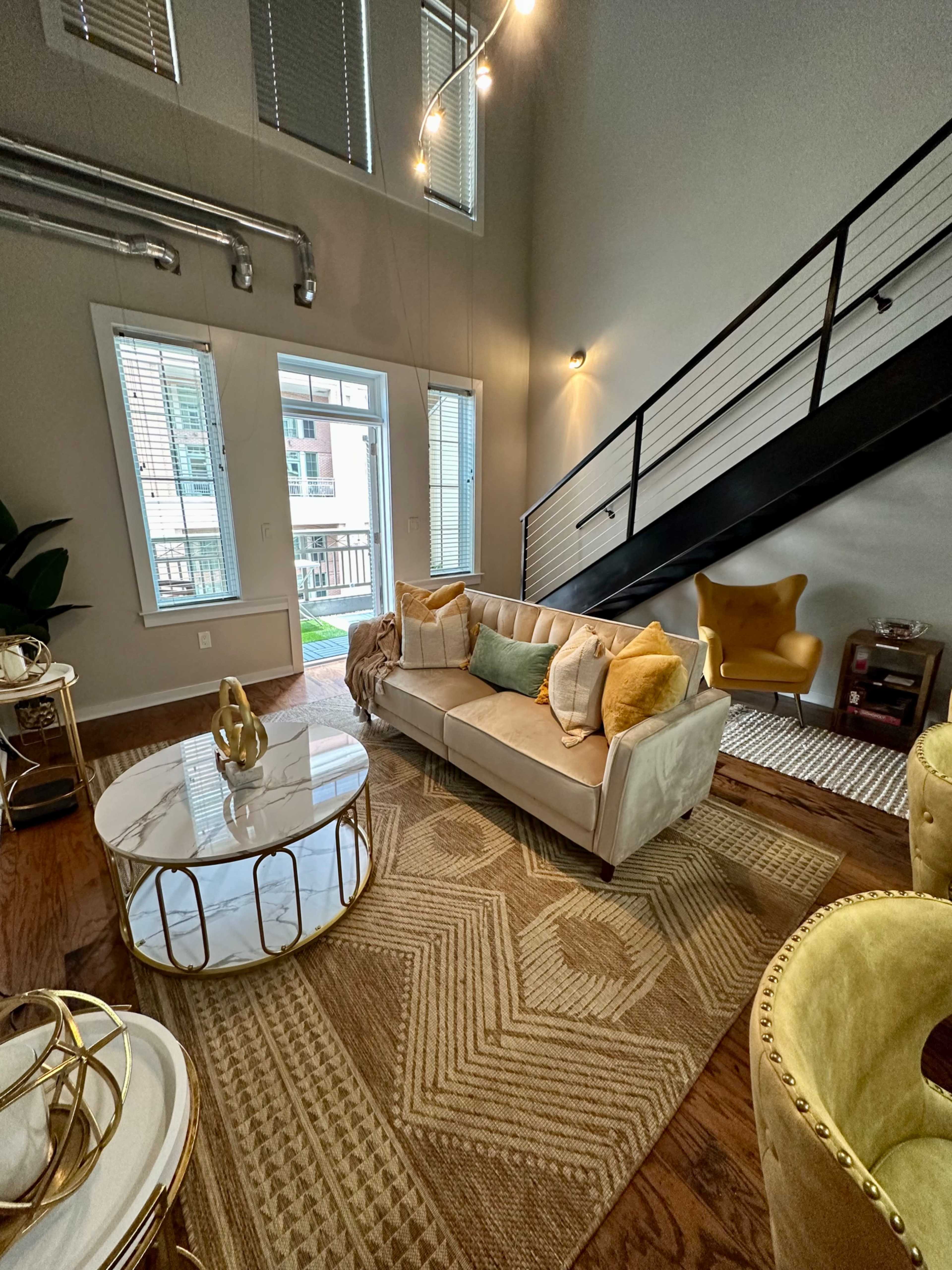 A modern living room featuring a light-colored sofa with decorative pillows, a round coffee table, and a staircase leading to an upper level.
