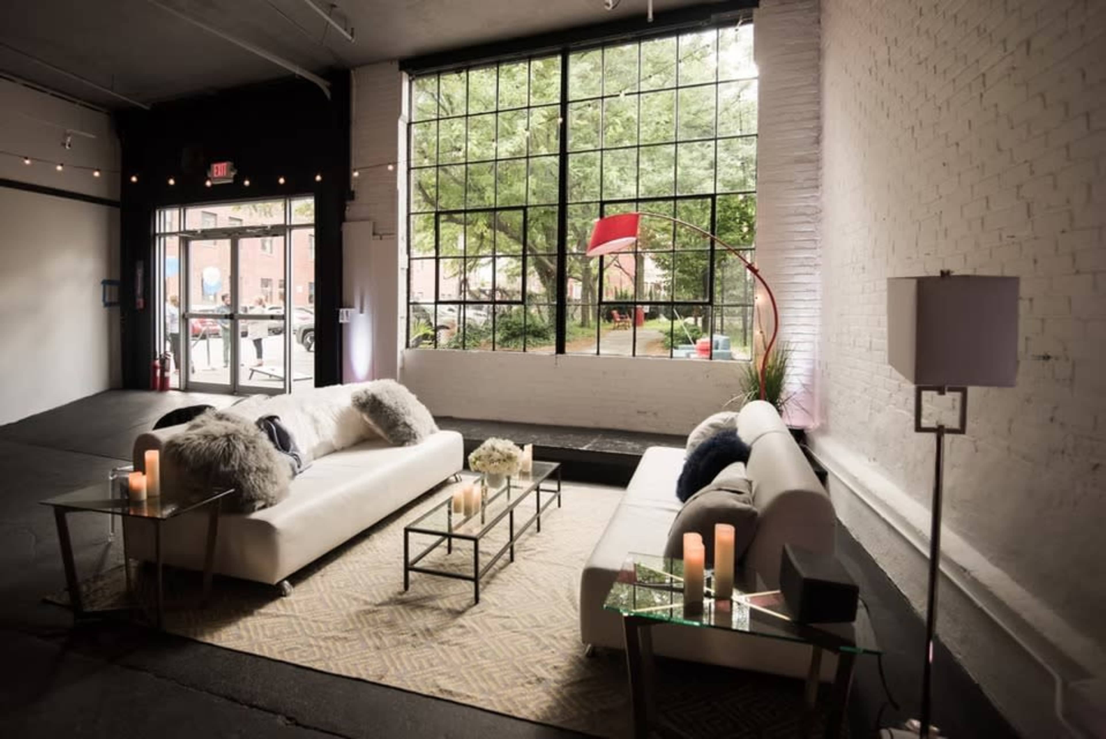 A spacious lounge area features two white sofas with decorative pillows, glass coffee tables, and large windows overlooking a green courtyard.