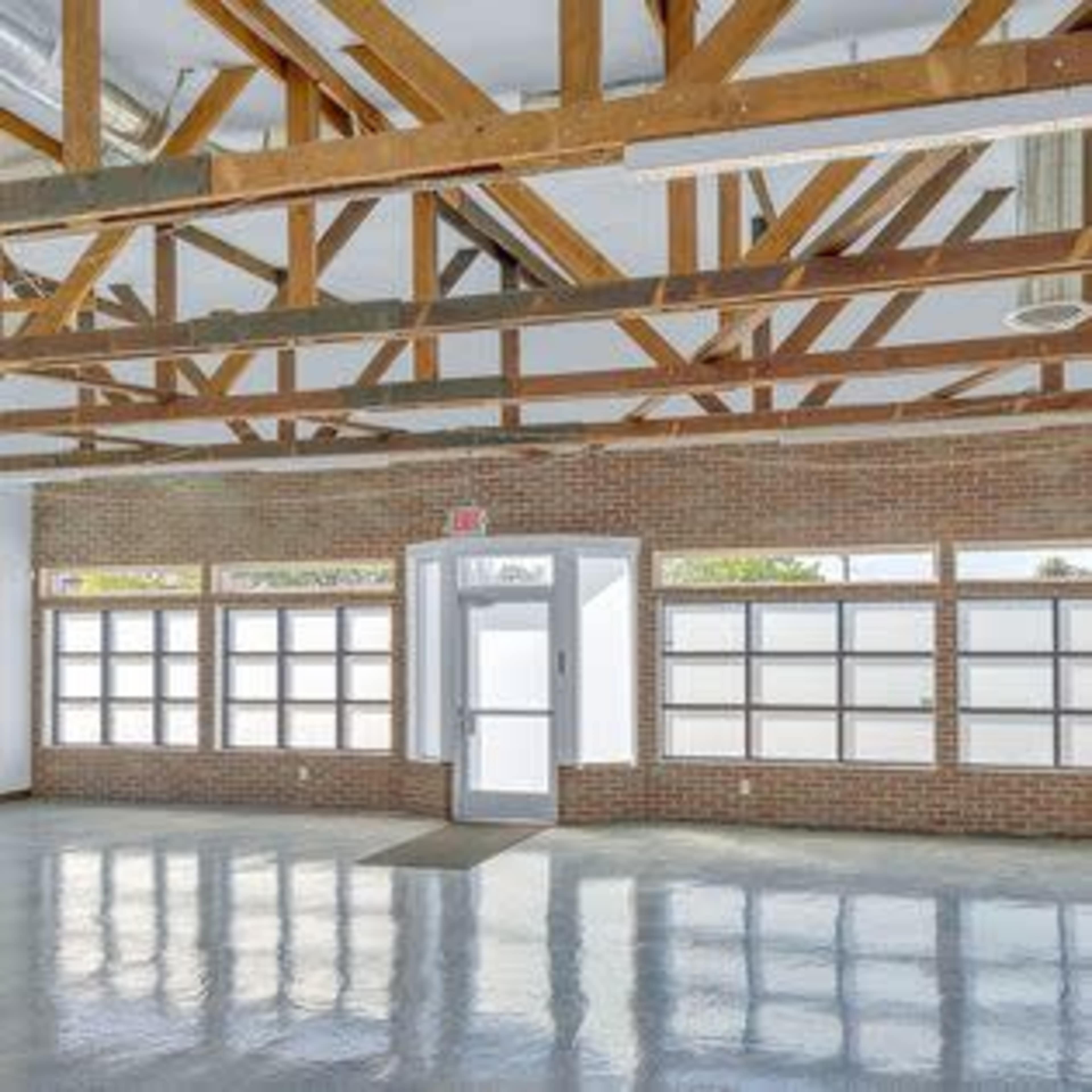 The image shows an empty room with polished flooring, large windows, and wooden beams in the ceiling.