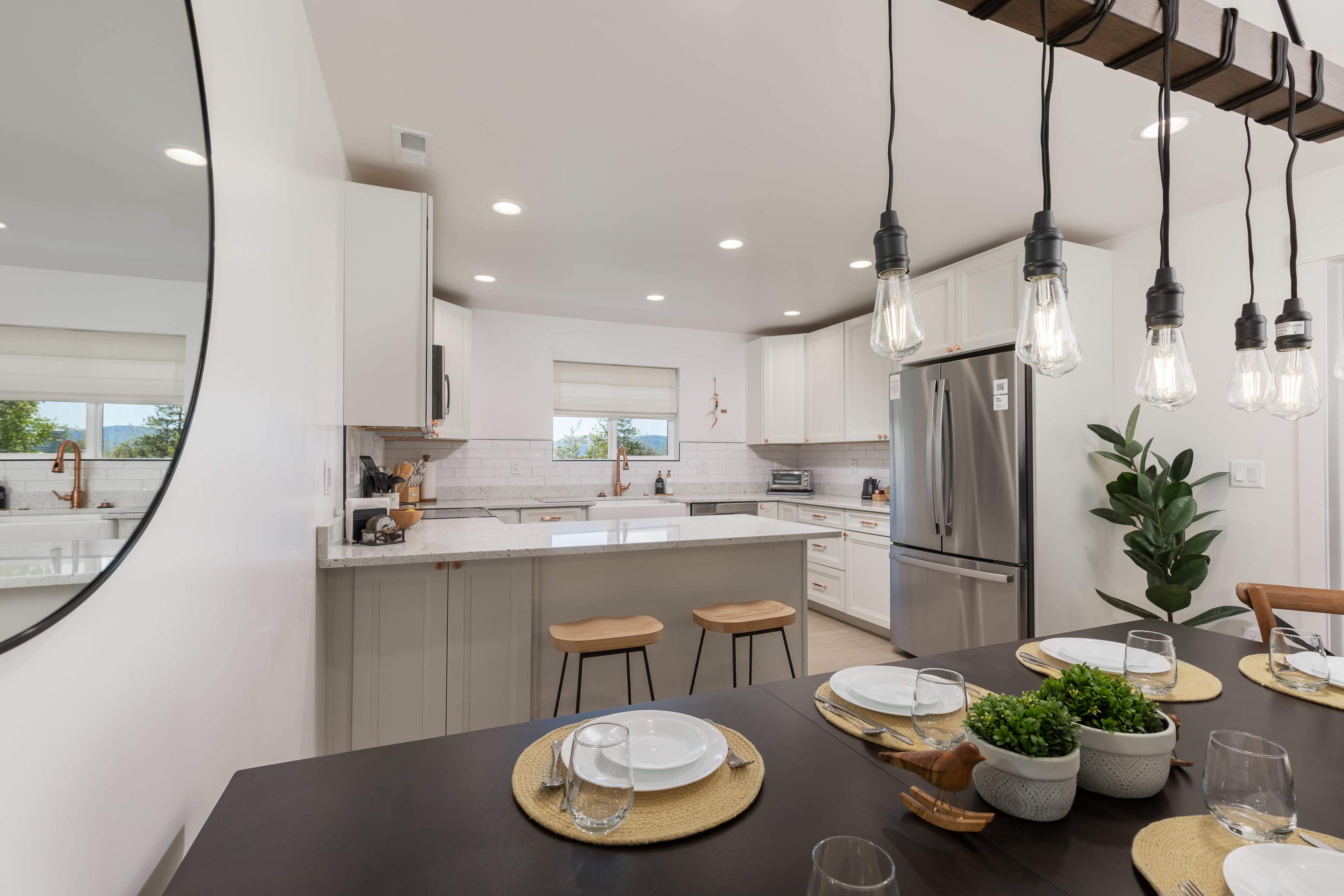A modern kitchen with white cabinetry, a central island with bar stools, and a dining table set for a meal.