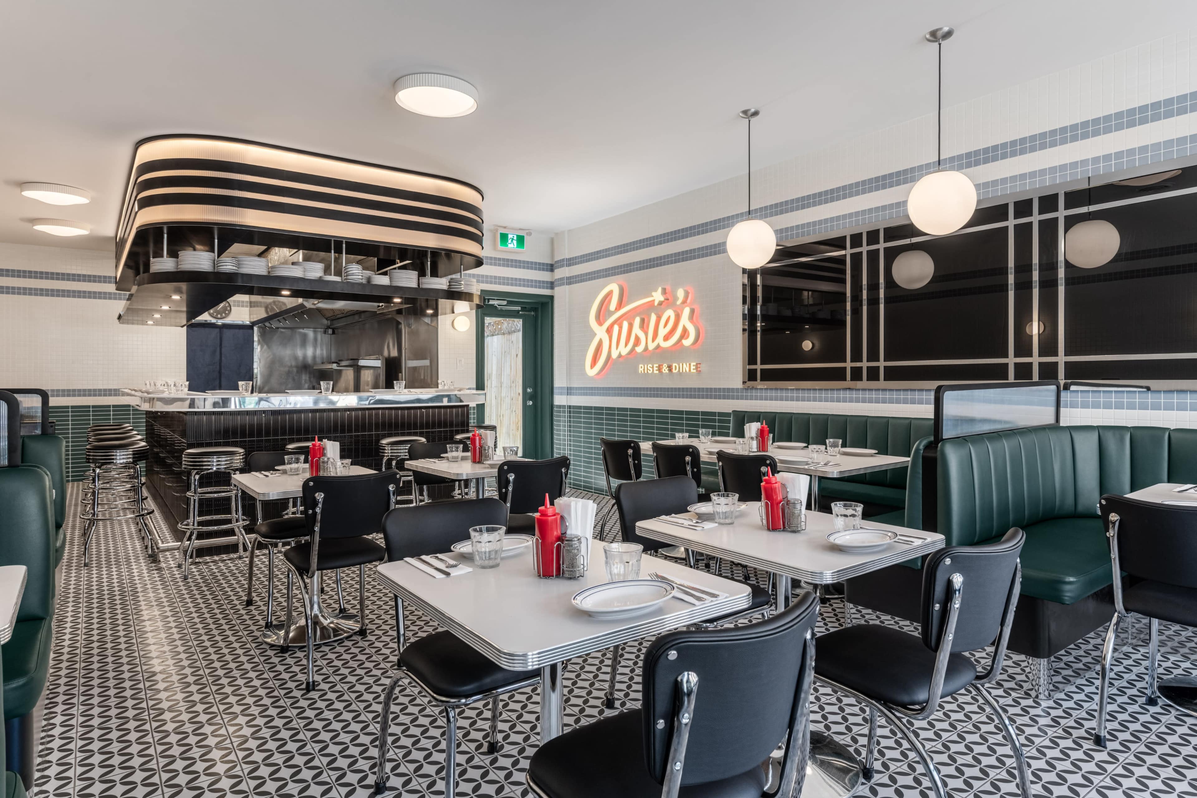 The image features a modern diner interior with booth seating, neatly arranged tables, and a kitchen area visible in the background.
